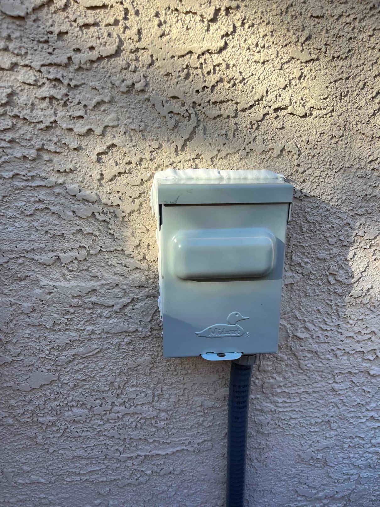 Weatherproof AC disconnect mounted on exterior stucco wall with flexible conduit routed into the enclosure.