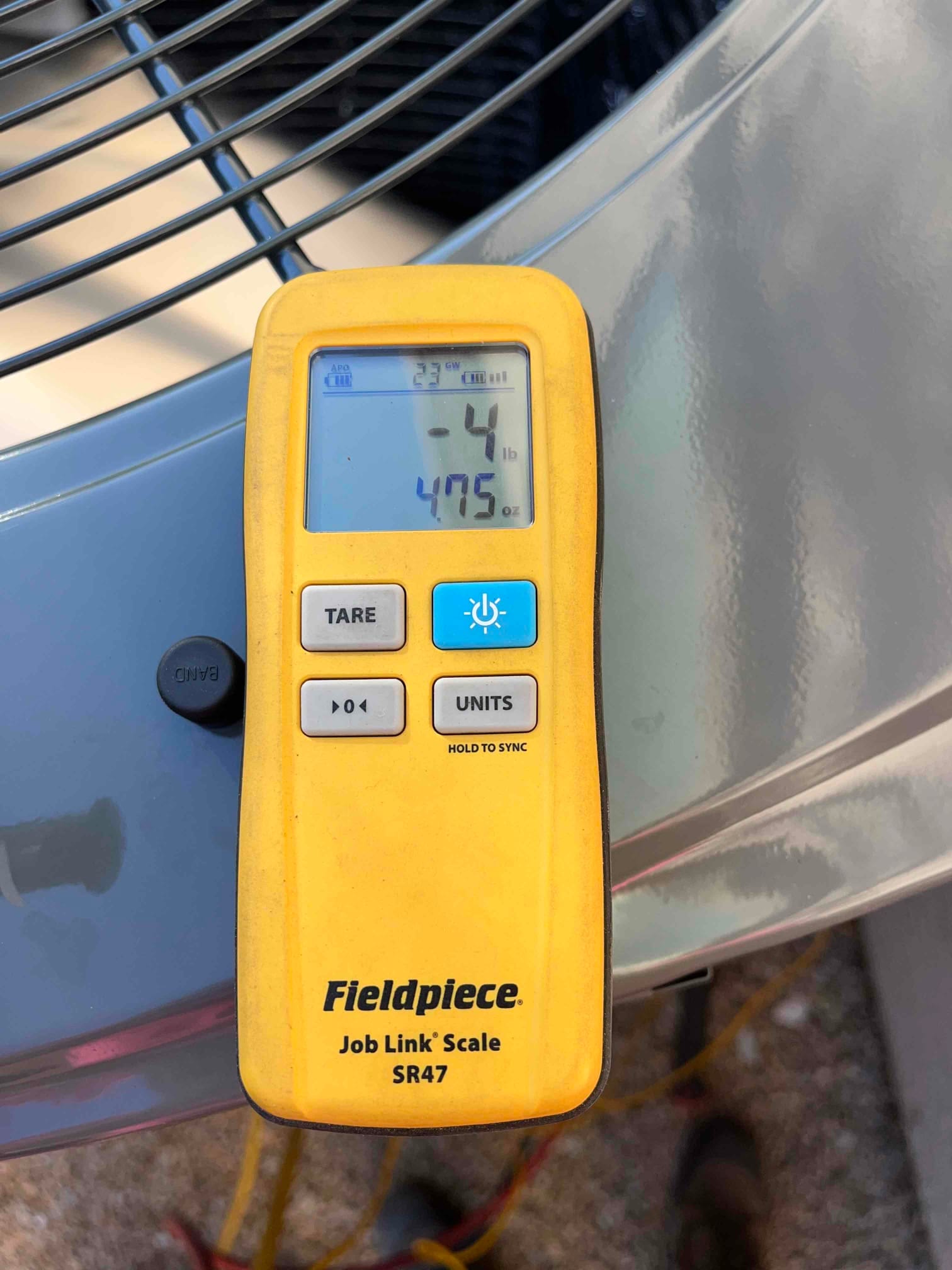 Wireless refrigerant scale remote shows -4 lb and 4.75 oz during charging work on the outdoor unit.