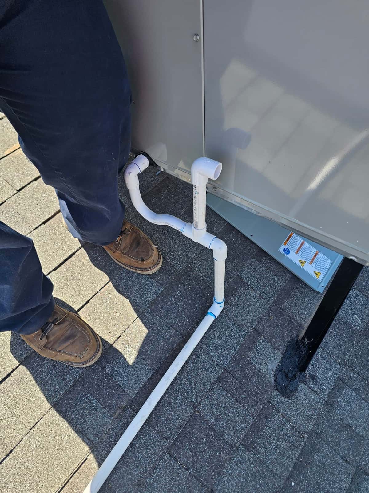 Condensate drain piping connected to a rooftop package unit, routed across shingles with glued PVC fittings and cleanout tee.