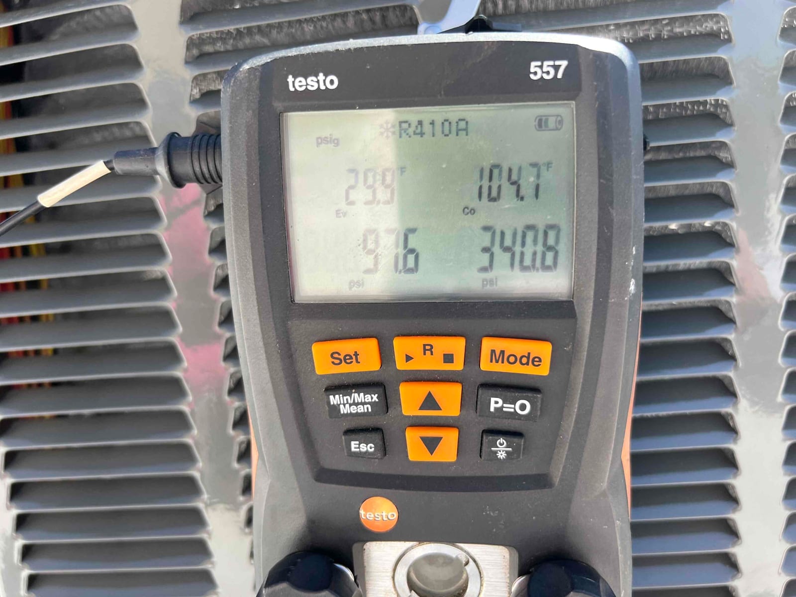 Digital manifold shows operating pressures on an outdoor condenser, with R-410A selected during commissioning checks.