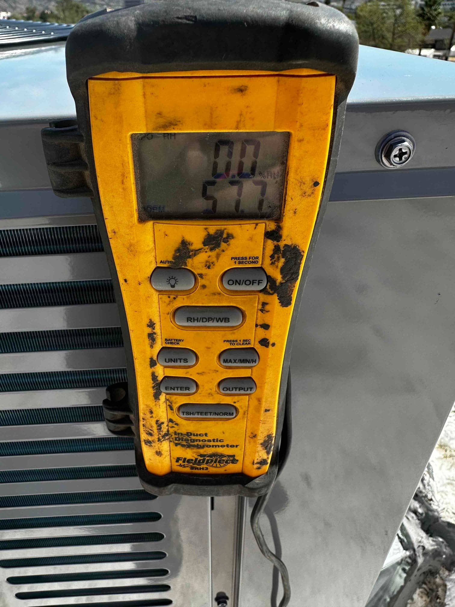Digital thermo-hygrometer clipped to outdoor unit shows 57.7 degrees Fahrenheit air temperature for supply measurement.