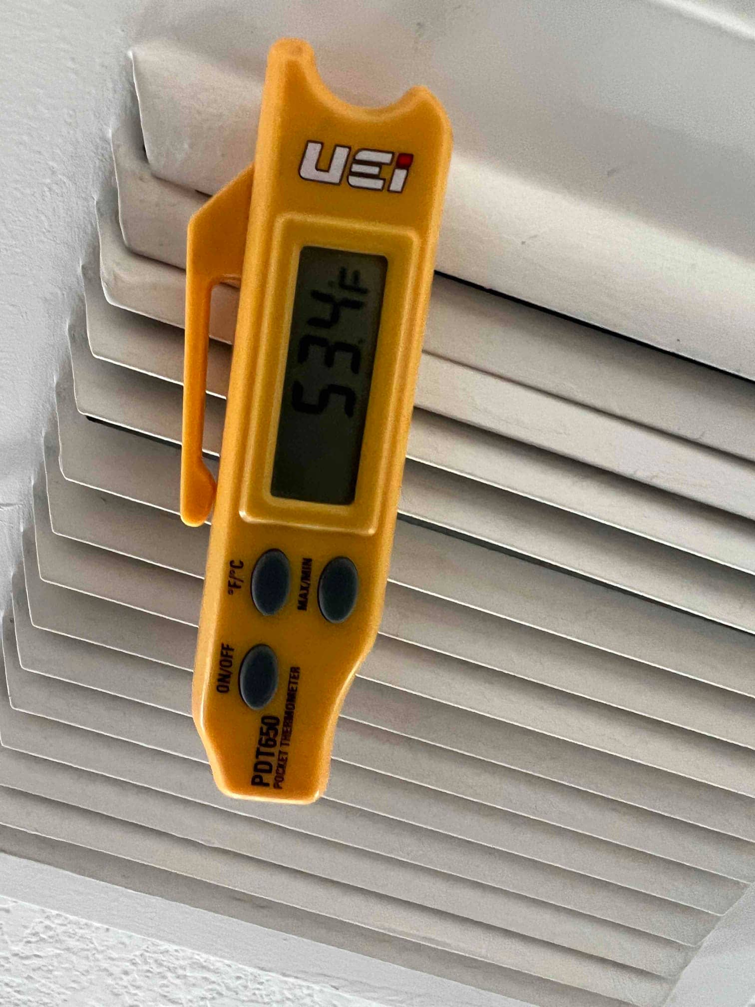 Digital thermometer clipped at a supply register shows 53.4°F, documenting cooled air temperature leaving the evaporator.