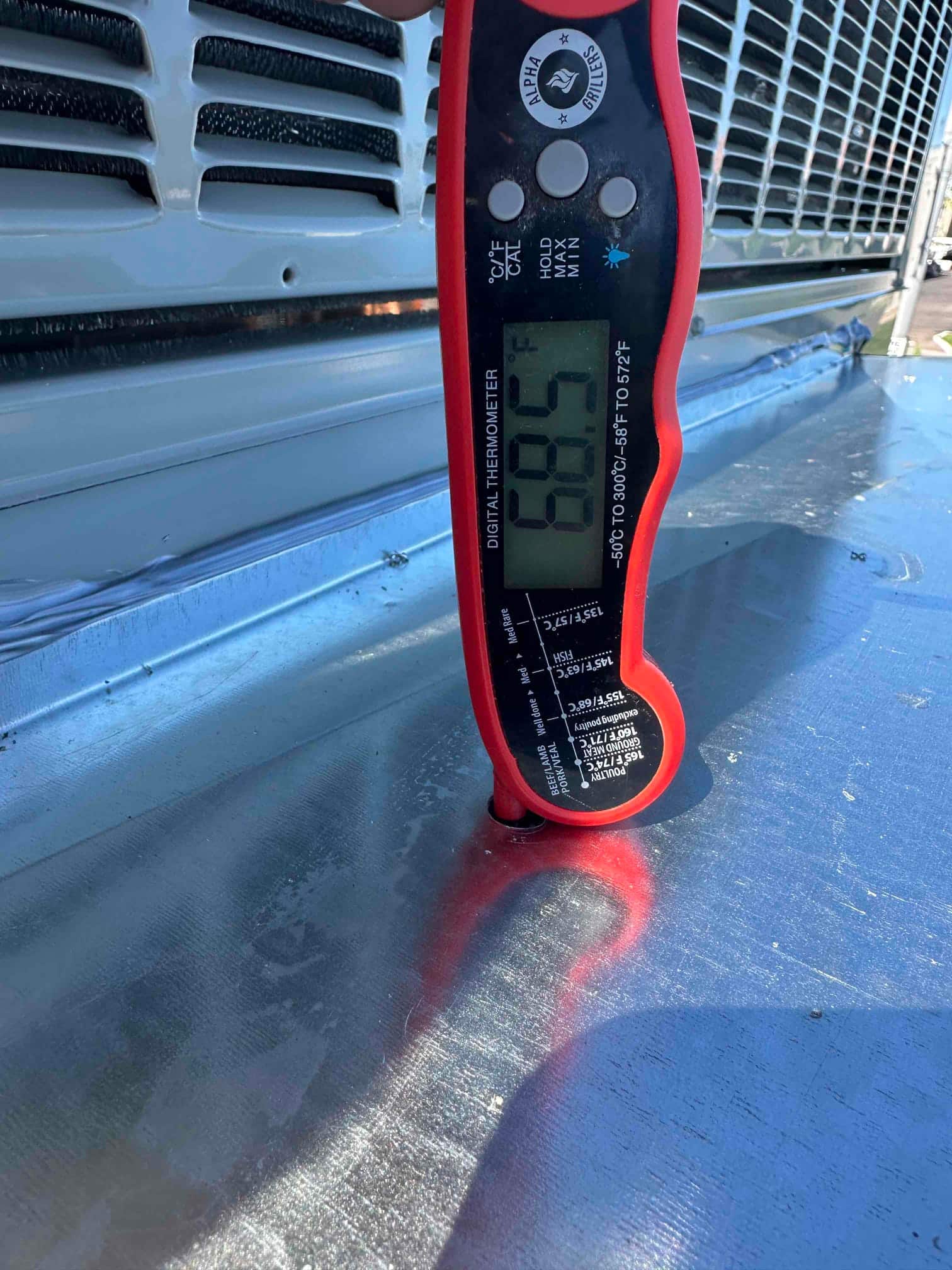 Digital thermometer inserted into ductwork reads 68.5°F, documenting an air temperature measurement during system commissioning.