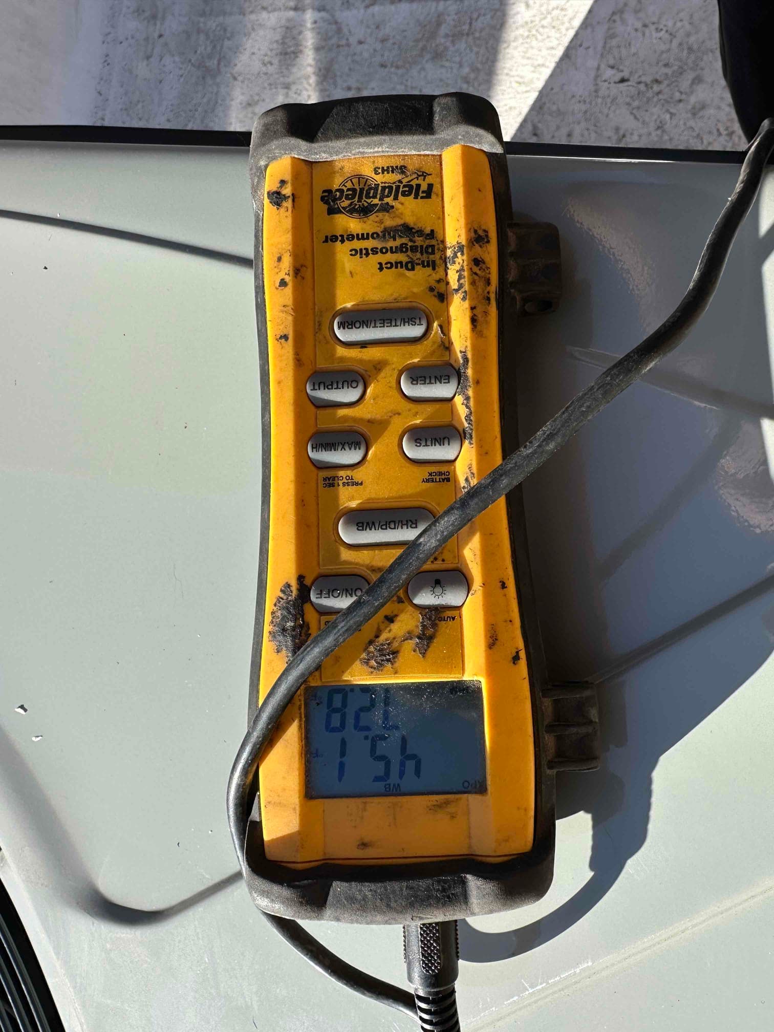 Digital thermometer with probe shows 82°F on the display during air temperature measurement at the HVAC system.