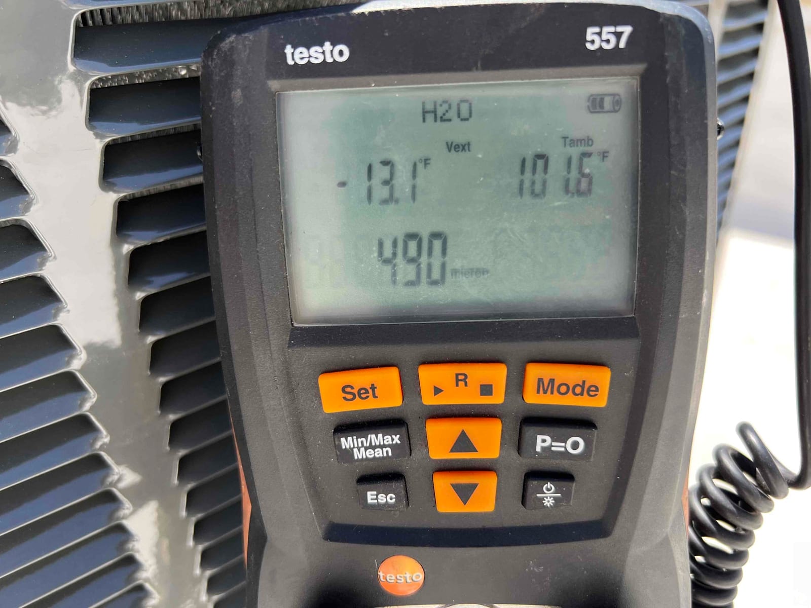 Digital vacuum gauge shows 480 microns during system evacuation beside the outdoor condenser cabinet.
