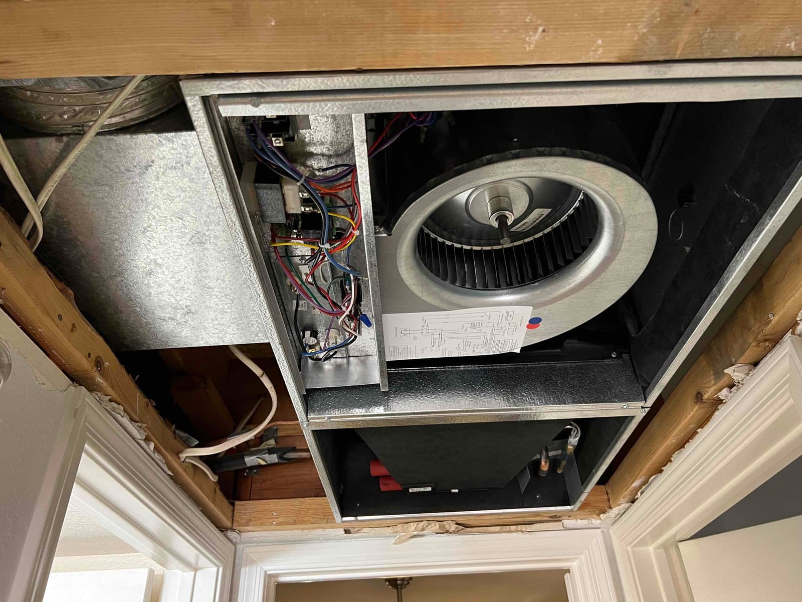 New ceiling-mounted air handler installed with blower assembly, control wiring compartment, and refrigerant connections visible within the open access panel.