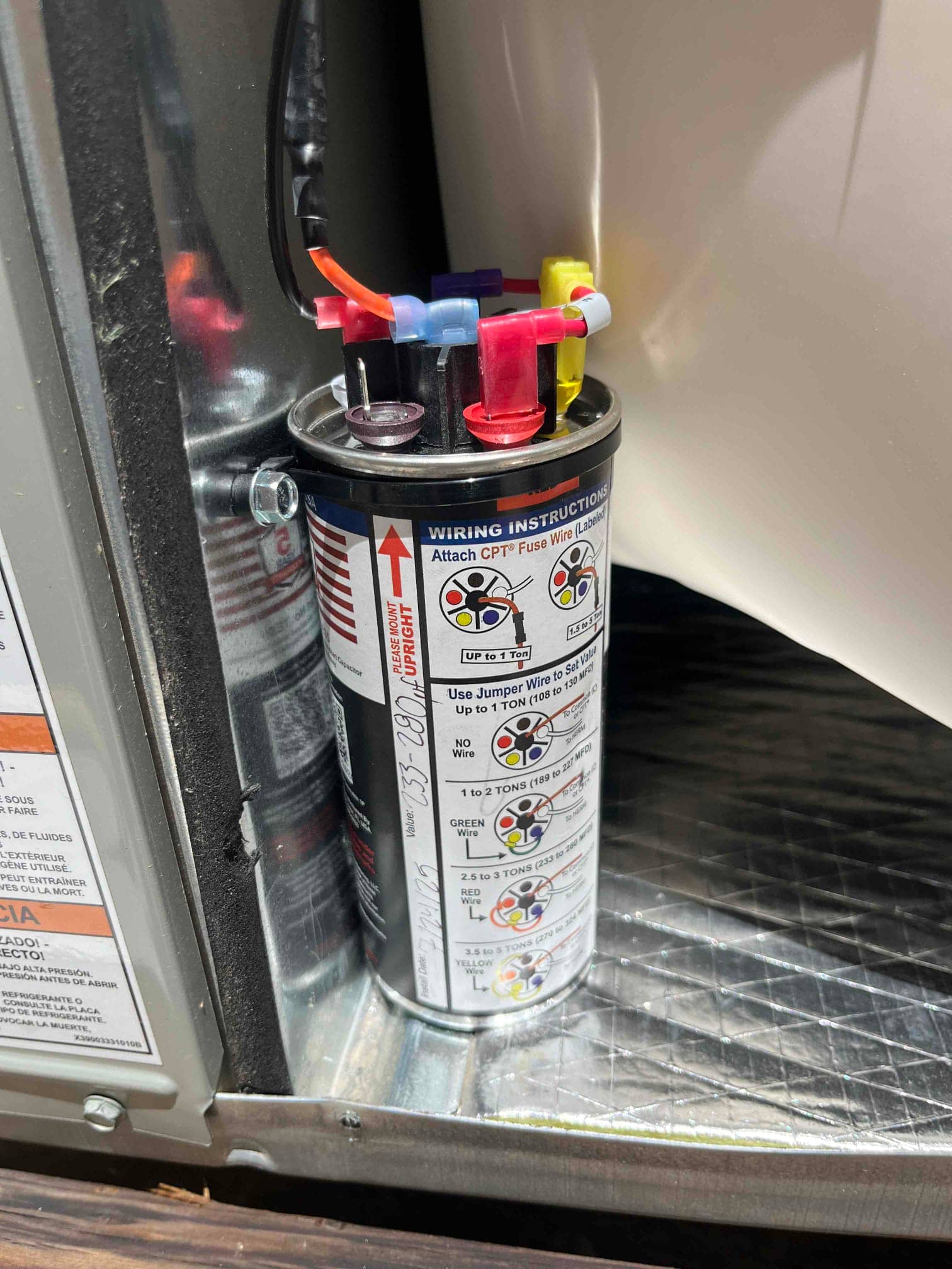 New hard start capacitor installed inside the condenser electrical compartment with labeled terminals and color-coded wiring connections visible.