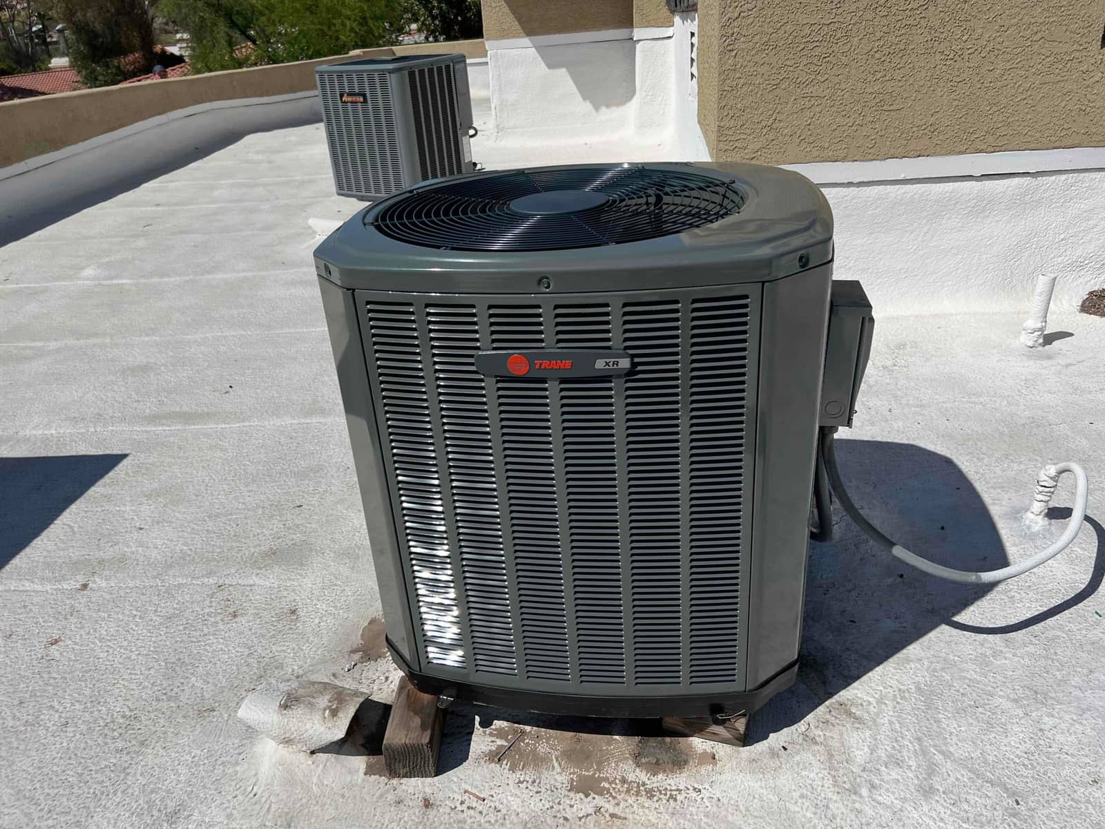 New outdoor condenser set on rooftop with insulated refrigerant line and nearby electrical disconnect mounted beside the unit.