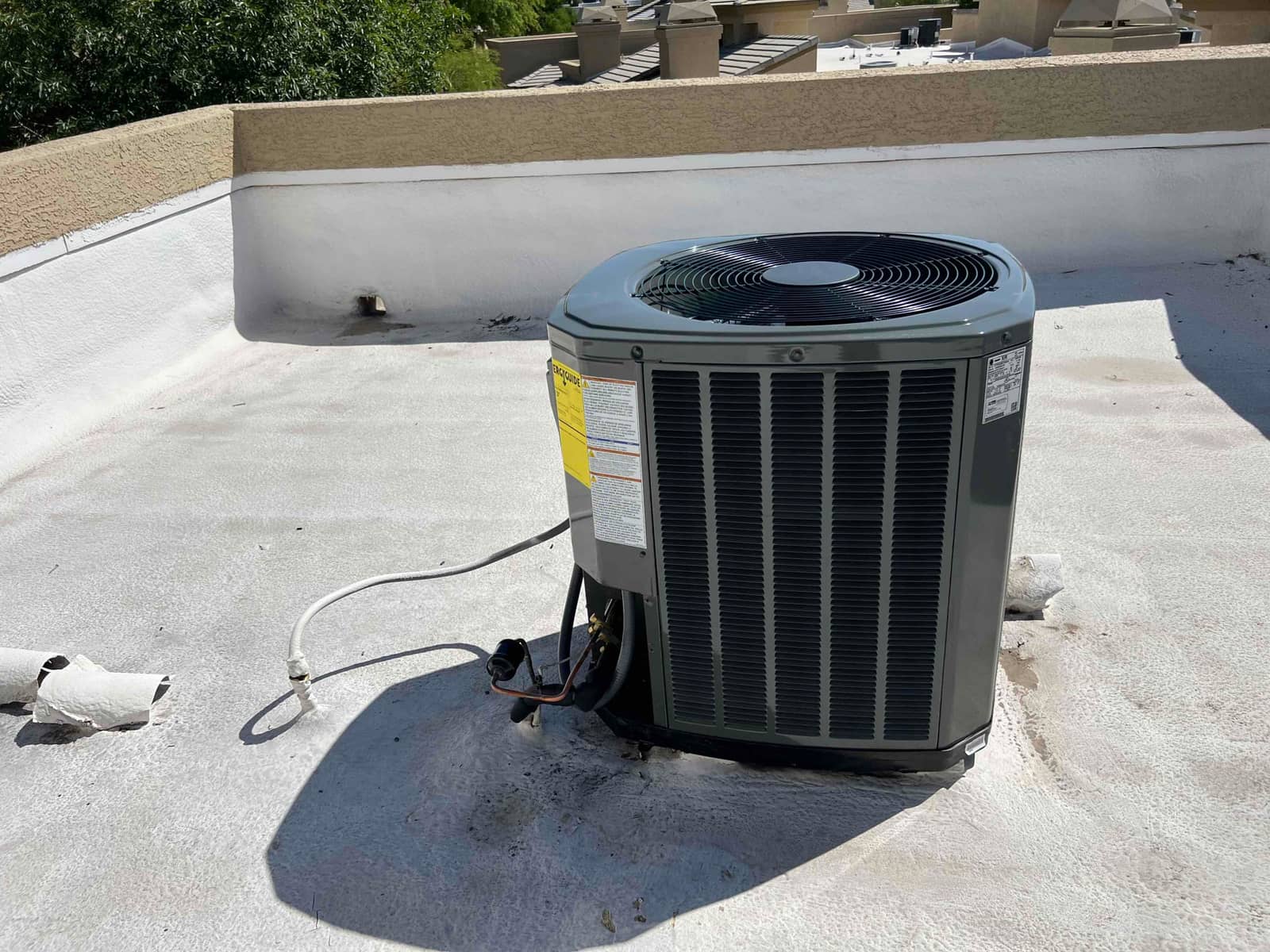 New outdoor condenser set on a rooftop surface with insulated refrigerant lines routed to the wall penetration.