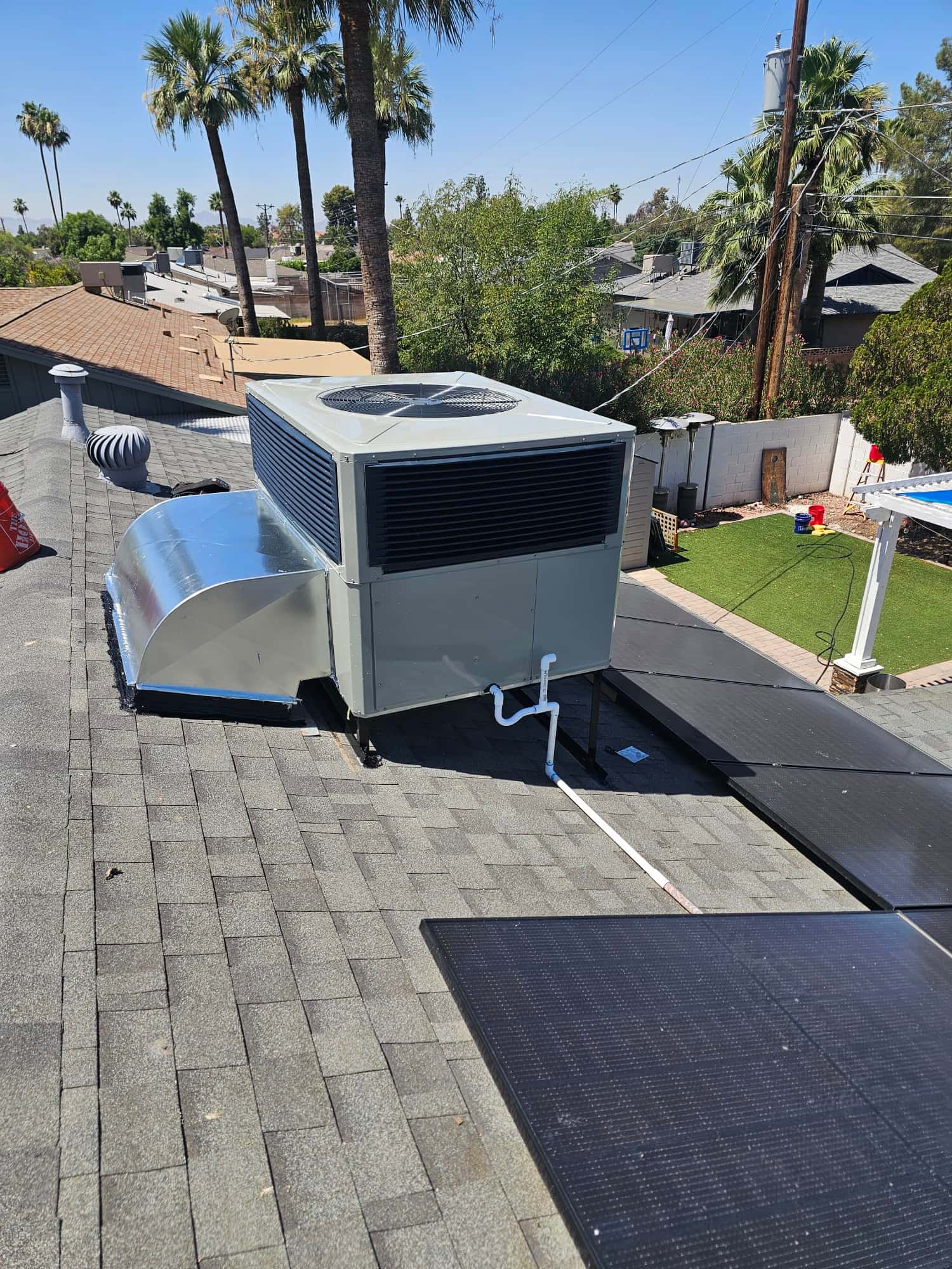 New rooftop package unit set on curb with sealed duct transition and condensate drain routed across the shingles.