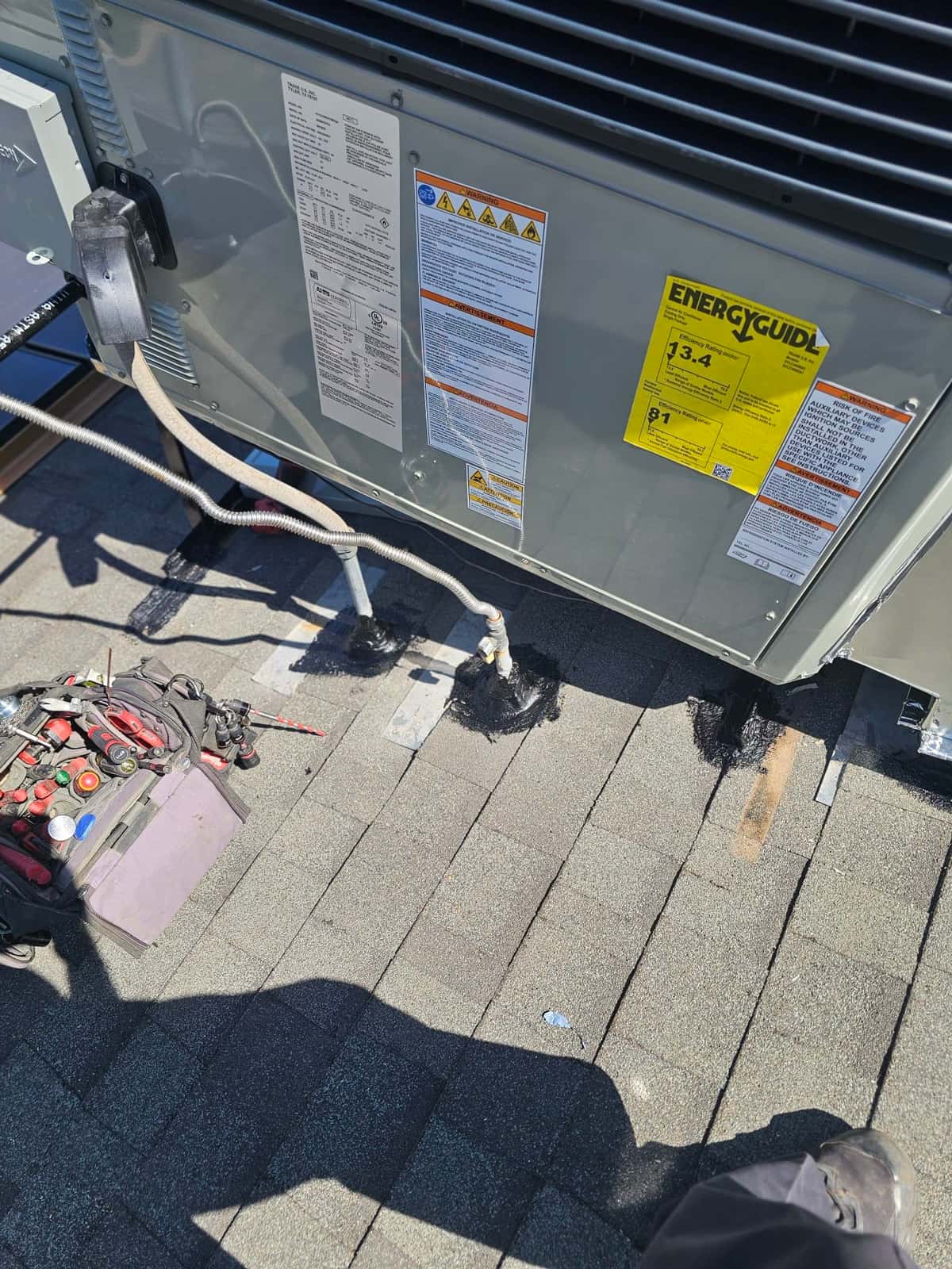 New rooftop package unit set in place with sealed roof penetrations and electrical whip connected; tools staged nearby for final commissioning.
