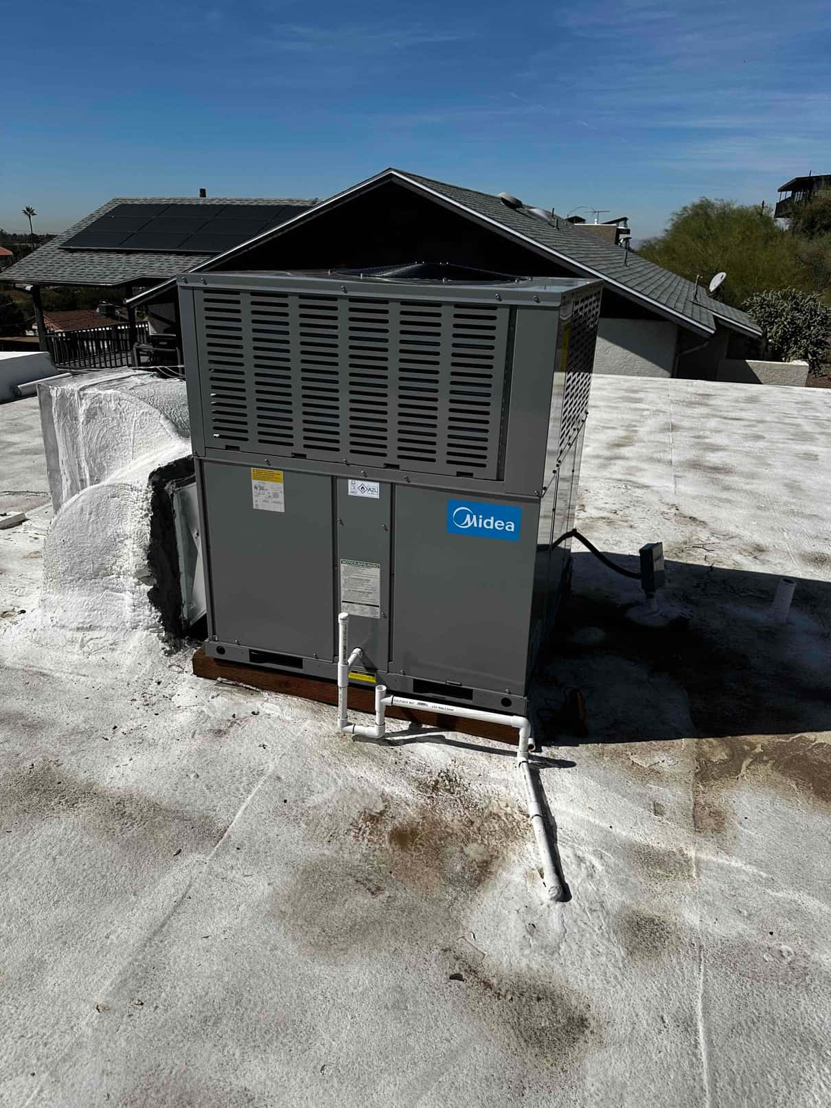 New rooftop packaged heat pump set on a level curb with connected condensate drain piping and sealed roof penetration.