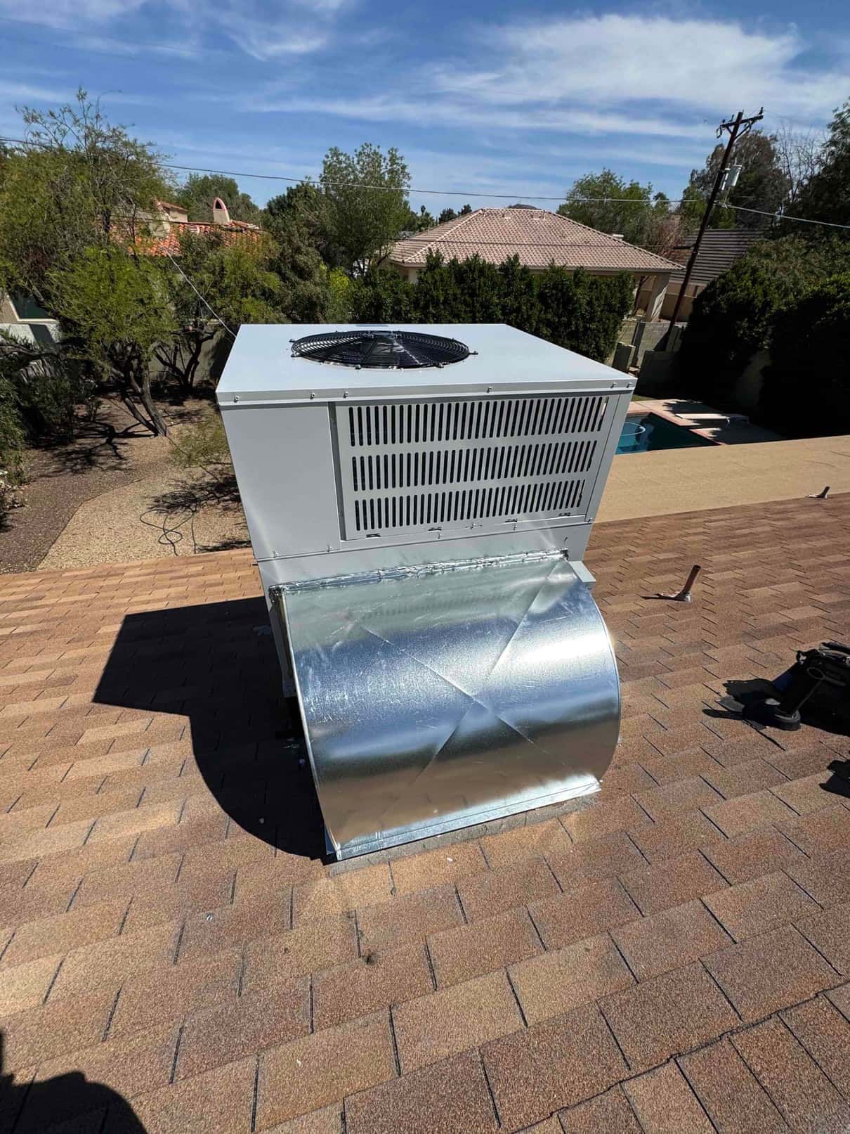 New rooftop packaged heat pump set on shingles with connected sheet metal supply plenum and rooftop curb transition.