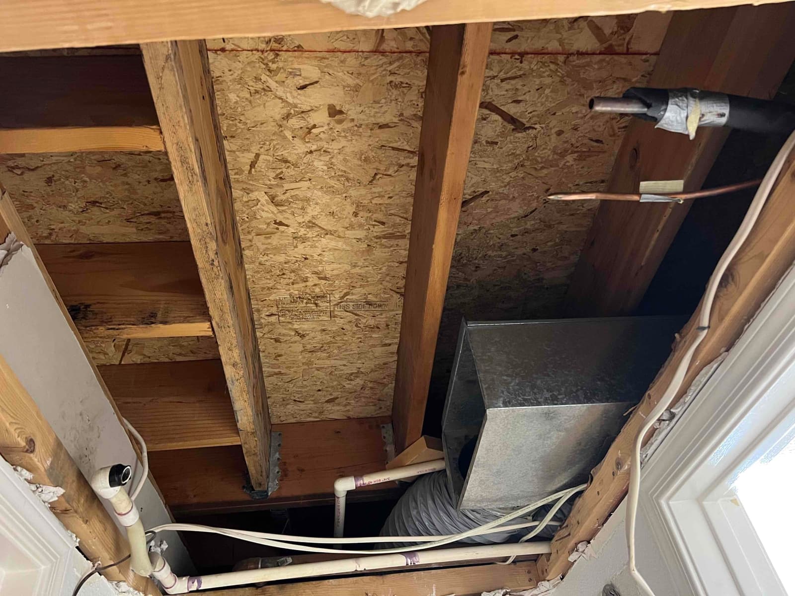 Open ceiling bay showing new duct connector, insulated flex duct, PVC condensate piping, and refrigerant lines routed through framing.