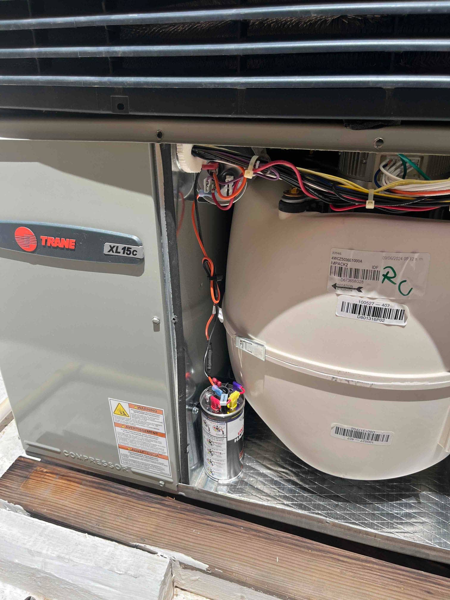 Outdoor condenser compartment open, showing newly installed dual-run capacitor with connected wiring and surge protector mounted beside the fan shroud.
