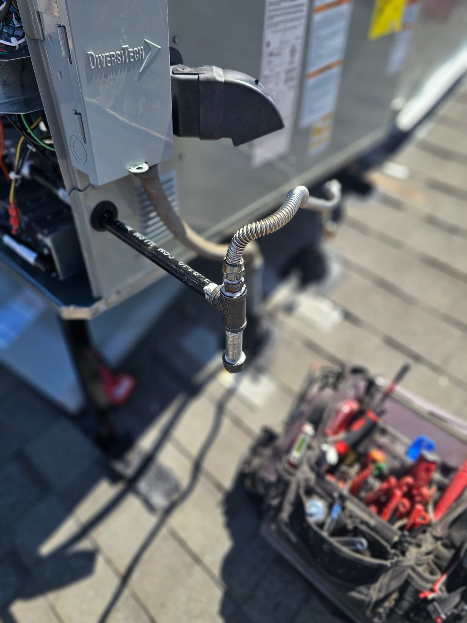 Outdoor disconnect and flexible conduit connected to the new rooftop package unit, with gas piping and service tools nearby.