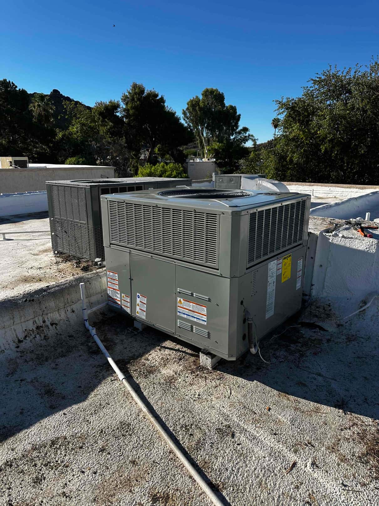 Rooftop package HVAC unit installed on a curb with condensate drain piping routed across the roof surface.