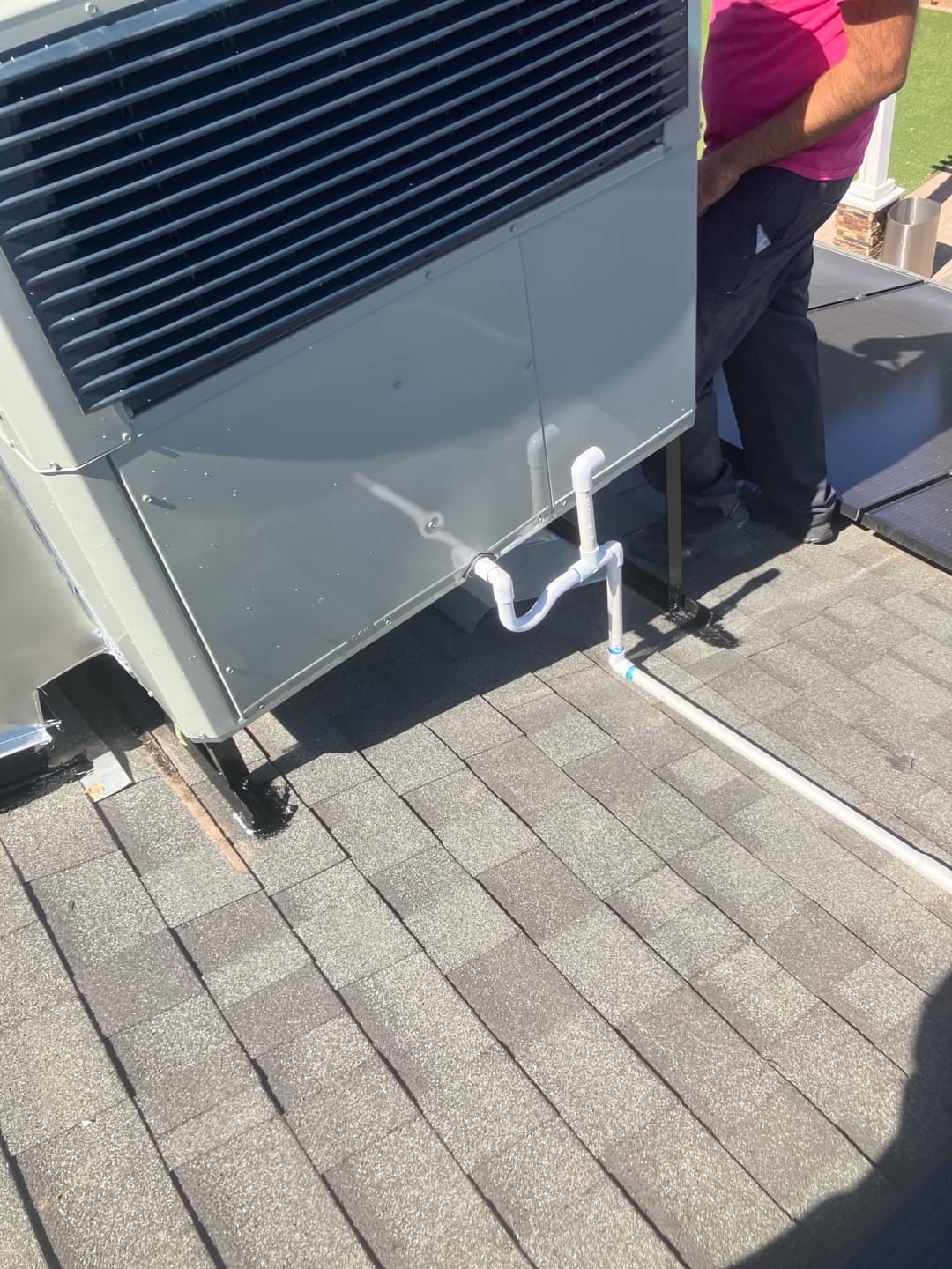 Rooftop package unit set on stands with newly installed condensate drain piping routed across the shingles.