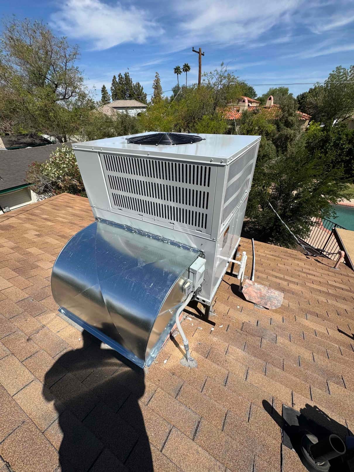 Rooftop packaged heat pump newly installed on shingles with curb duct connection, electrical whip, and sealed penetrations visible.
