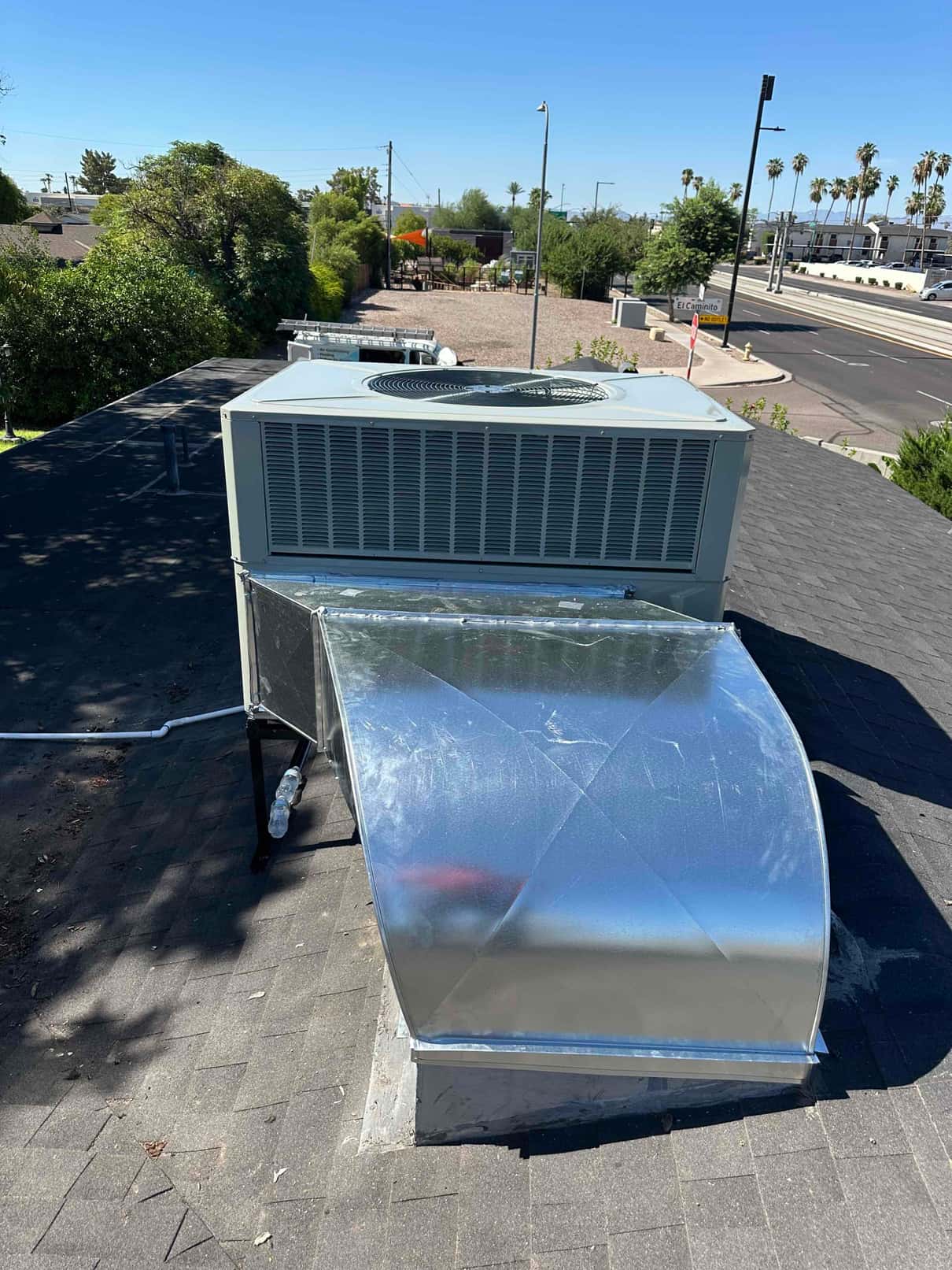 Rooftop packaged HVAC unit newly installed on curb with sealed sheet-metal duct transition and insulated condensate drain on the roof.