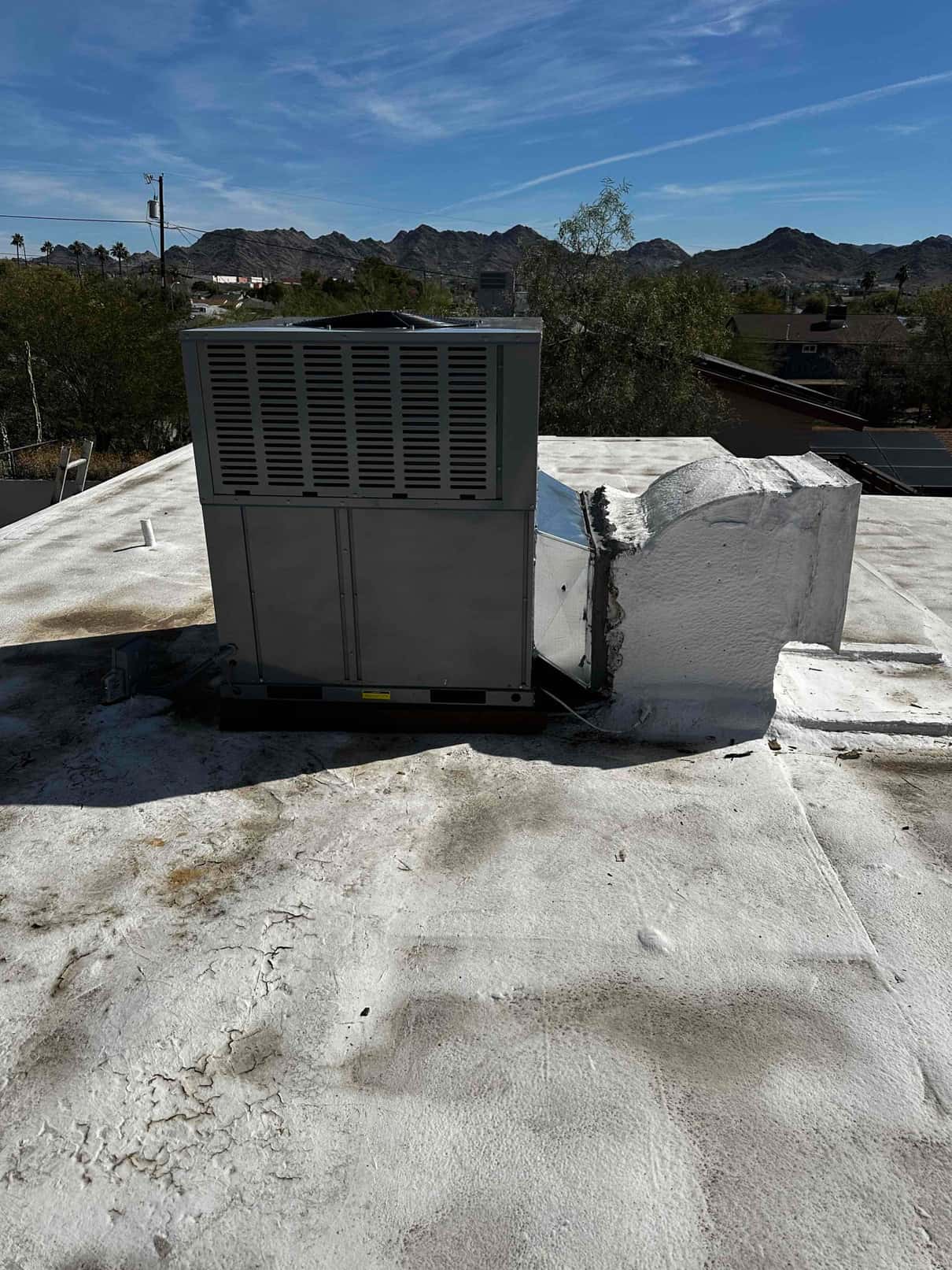 Rooftop packaged HVAC unit newly set on curb with connected supply and return duct transitions on a flat roof.
