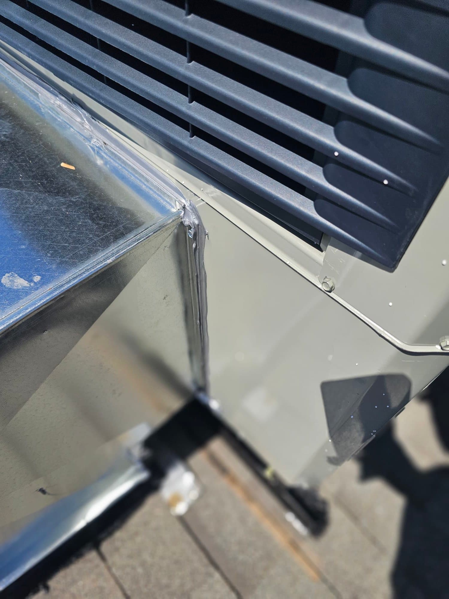 Sheet metal duct transition sealed to the side of a rooftop package unit, with mastic applied along the joint.