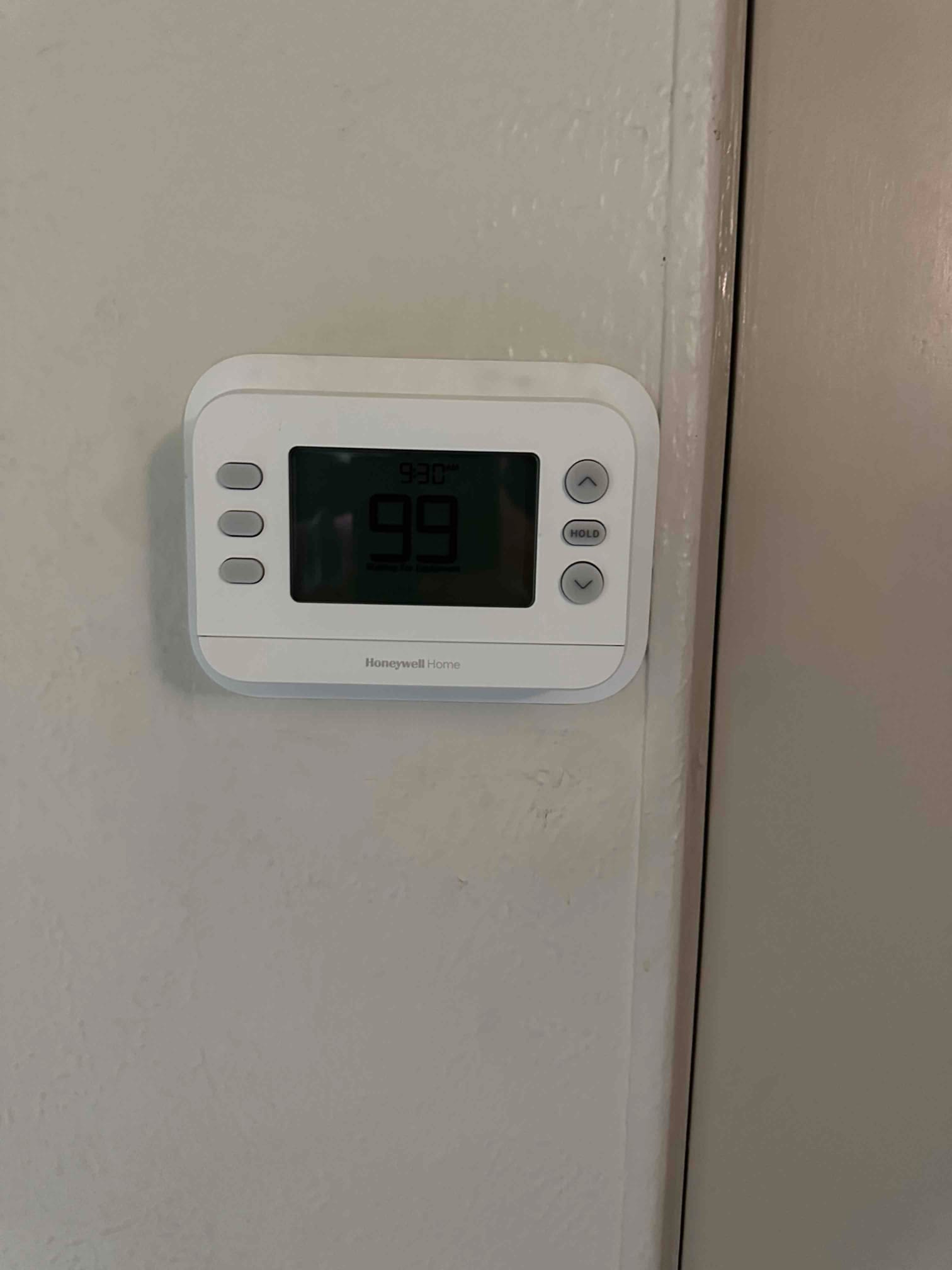 Wall-mounted digital thermostat installed and powered, displaying room temperature and control buttons for system operation.