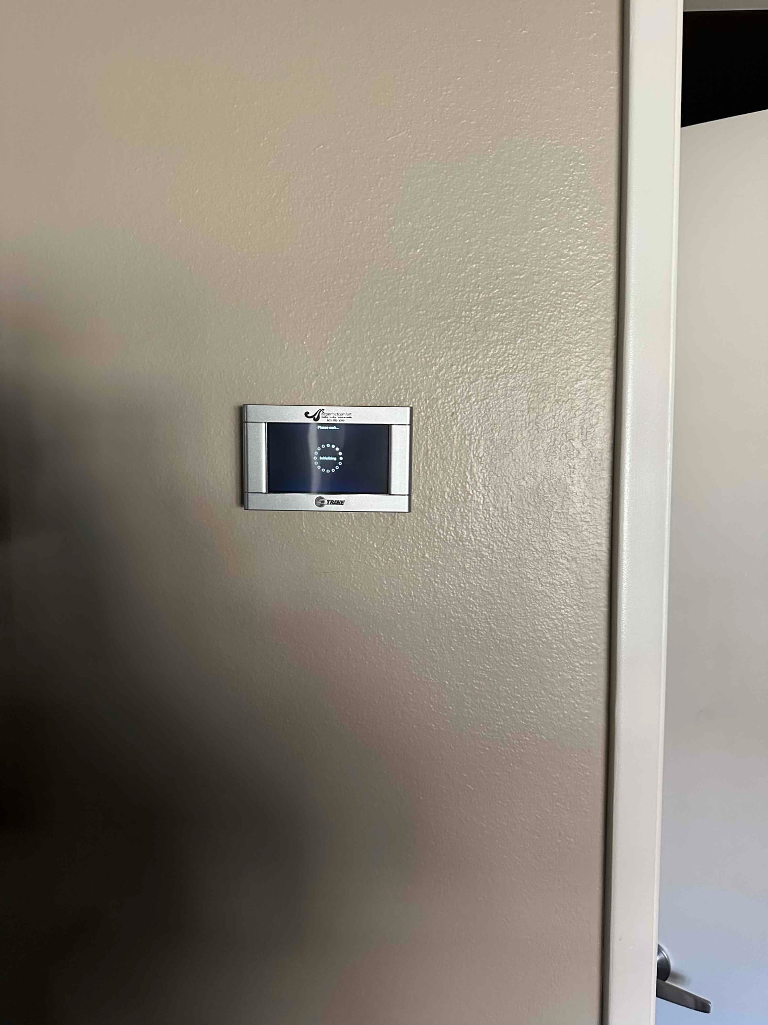 Wall-mounted thermostat installed on a finished interior wall, displaying a circular loading indicator on its screen.