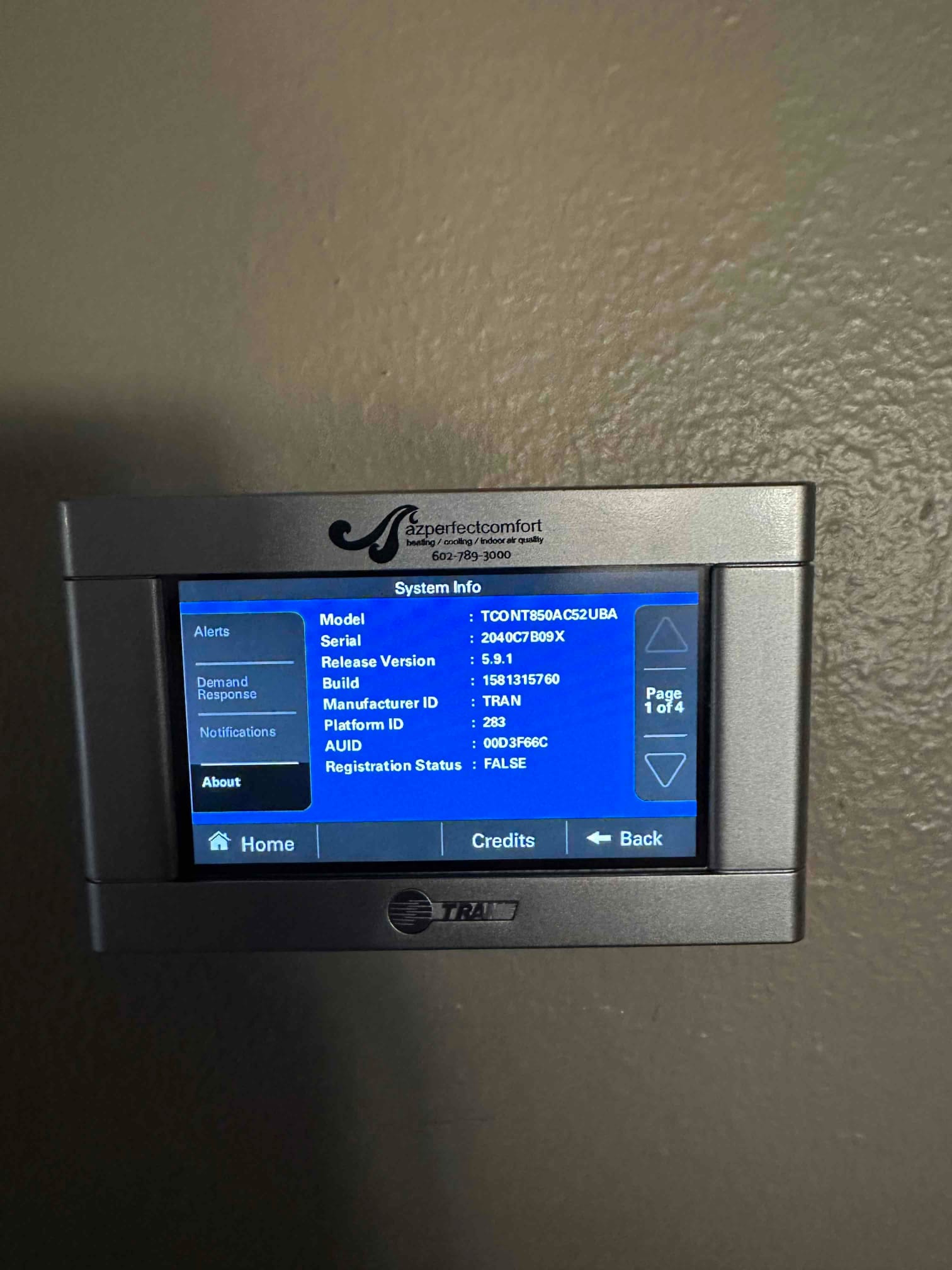 Wall-mounted touchscreen thermostat displaying system information menu after installation, showing navigation buttons and a blue information screen.