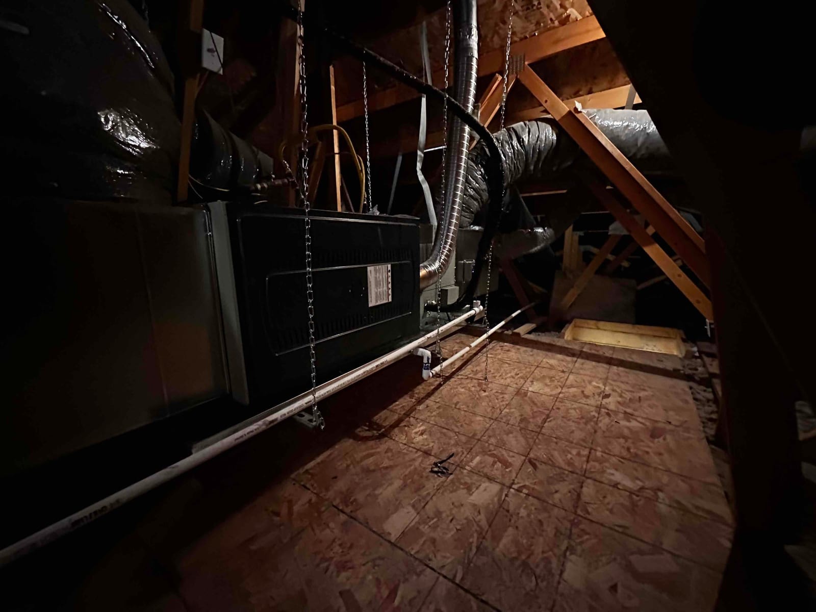 Air handler hung in an attic with insulated duct connections, condensate drain piping, and service platform visible along the walkway.