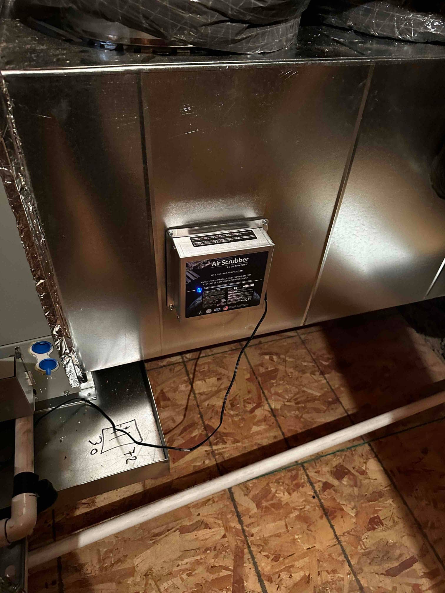 Air handler with an installed air scrubber accessory mounted on the supply plenum, drain line and insulated duct connections visible.