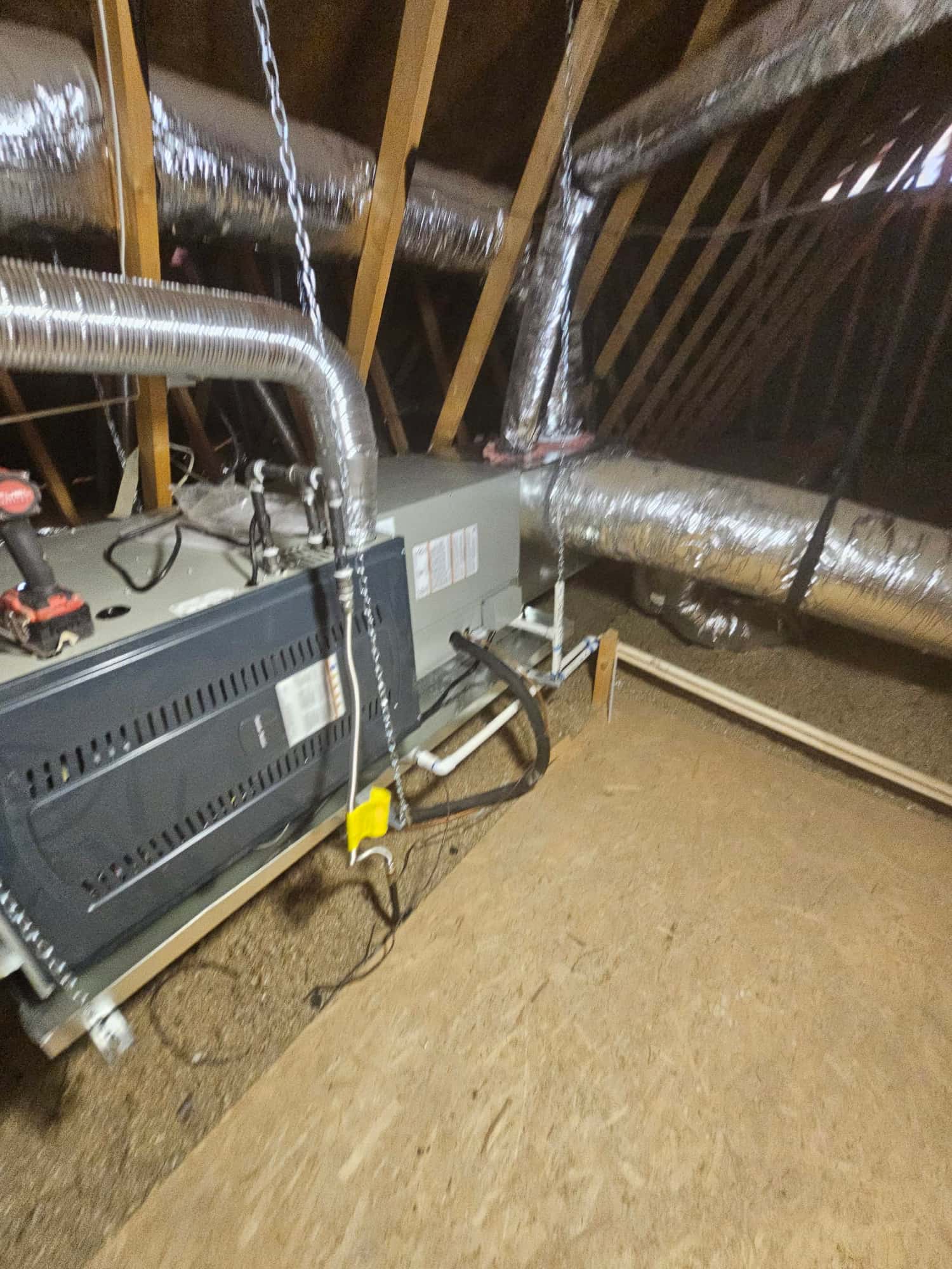 Air handler installed on a suspended platform in the attic with insulated ductwork, drain piping, and refrigerant lines connected.
