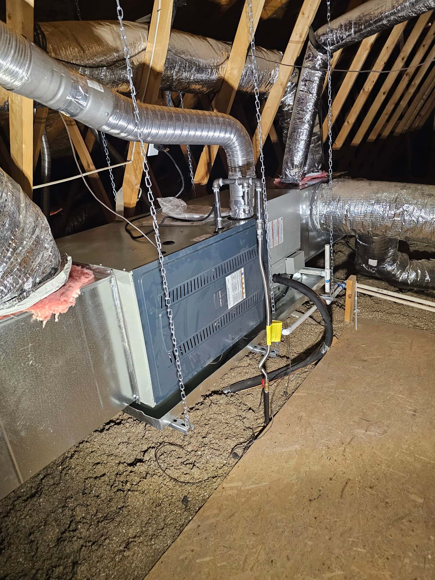 Air handler suspended in attic with connected supply and return ducts, condensate drain, and insulated refrigerant line set.