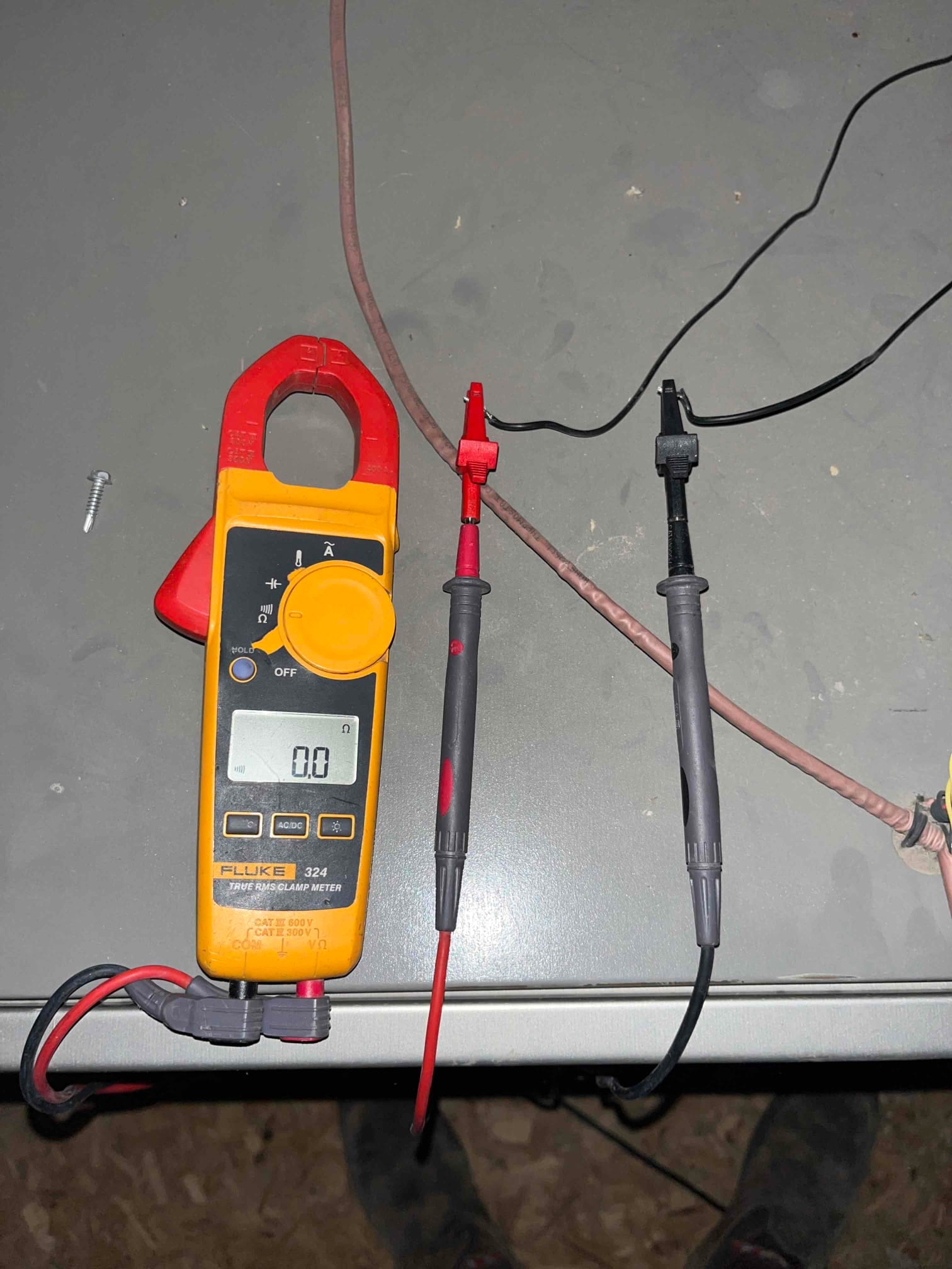 Clamp meter displays 0.0 V while test probes are connected to leads on the workbench.