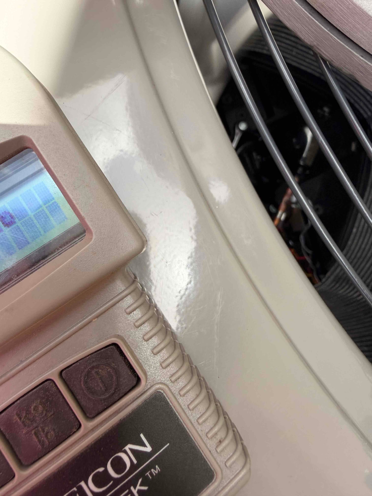 Close-up of a handheld digital device resting on the outdoor condenser top near the fan guard.