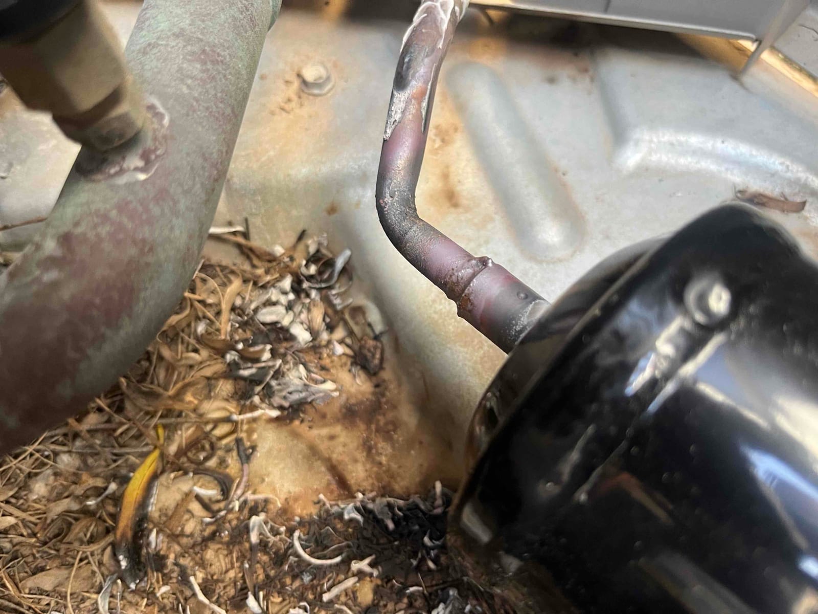 Close-up of a newly brazed refrigerant line connection at the compressor, showing fresh solder and surrounding condenser base.