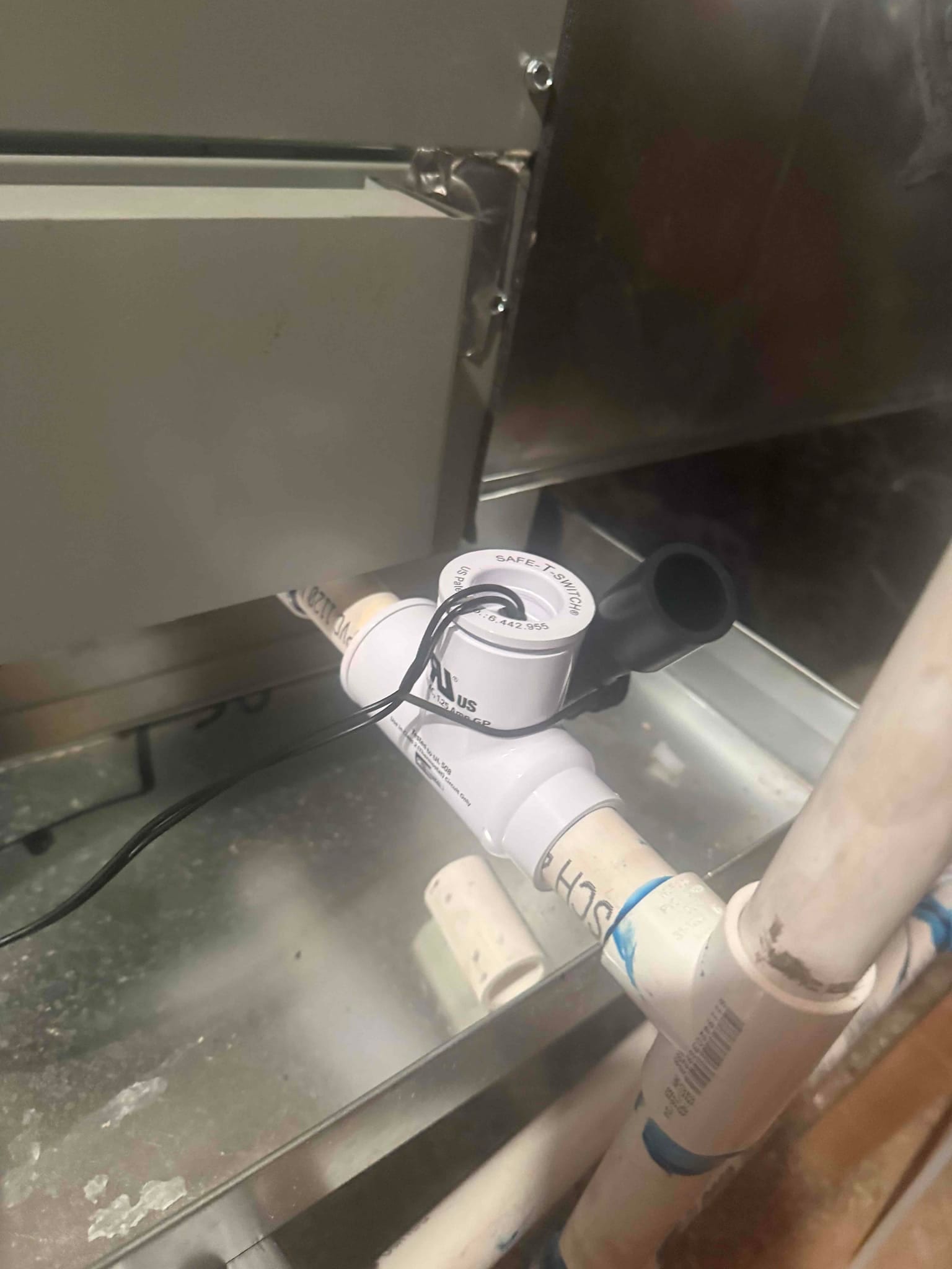 Condensate drain assembly with inline float safety switch installed on PVC near the air handler cabinet.