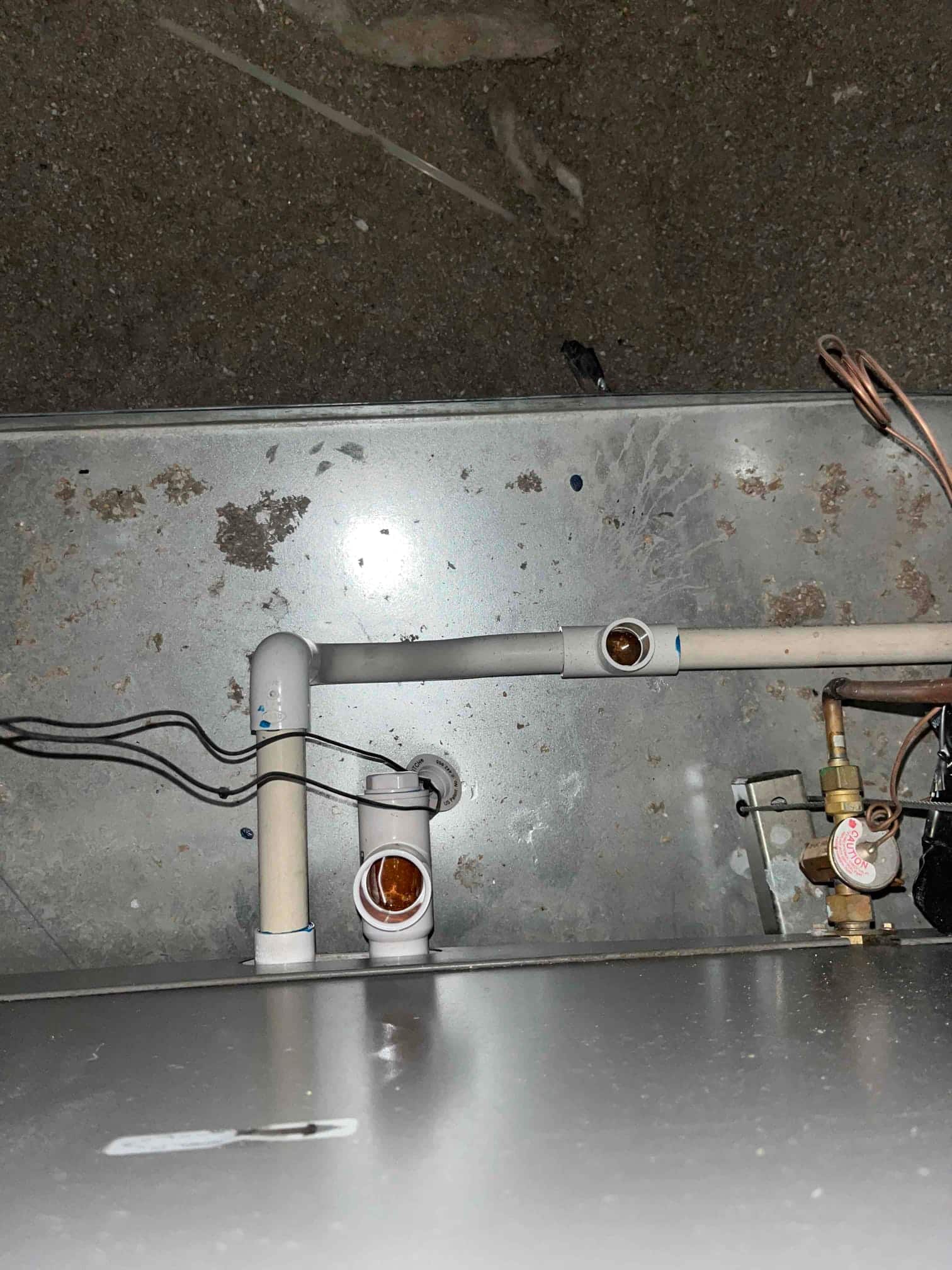 Condensate drain line assembly at an air handler, showing cleanout tees, float switches, PVC piping, and connected wiring.