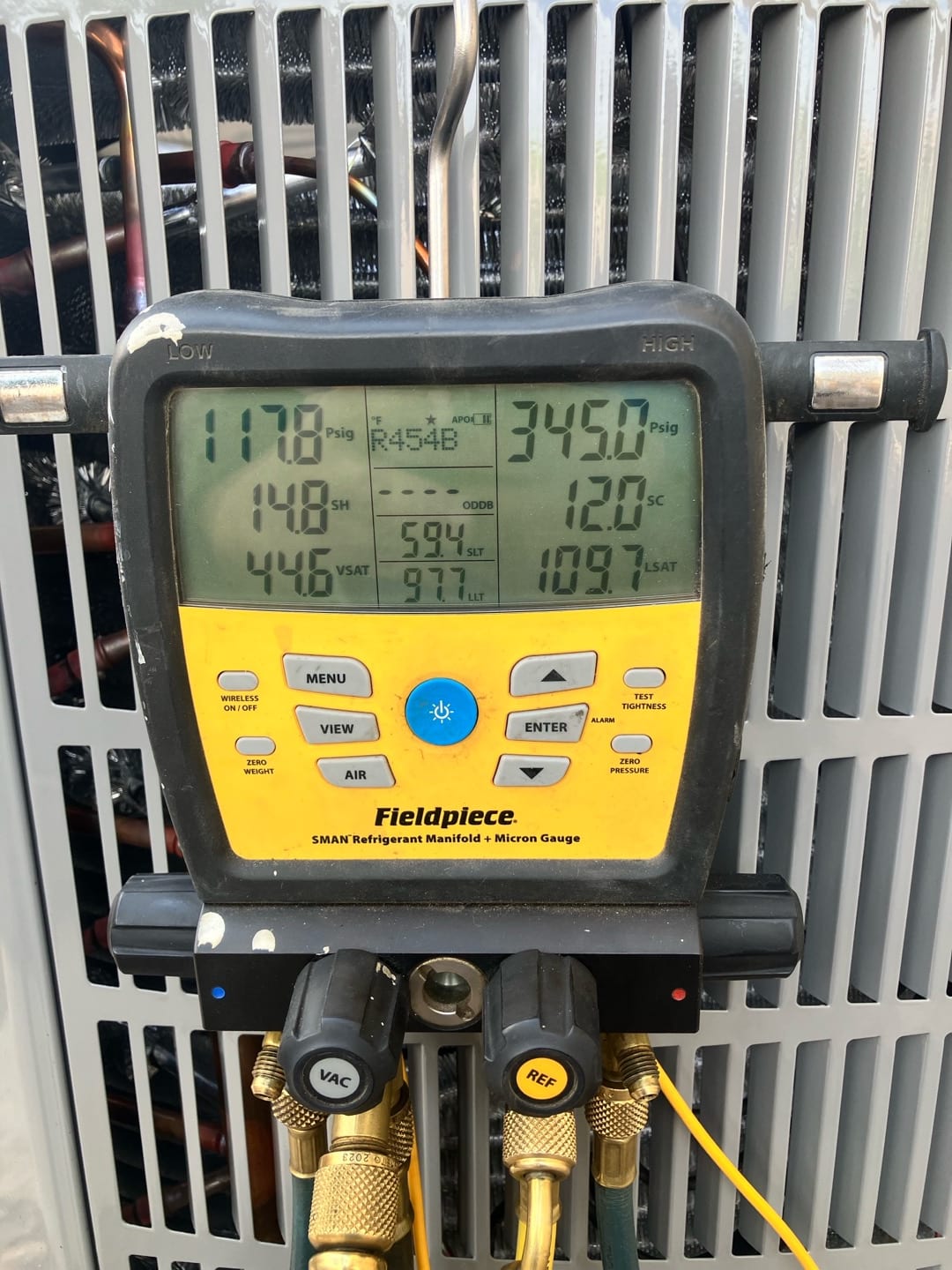 Digital manifold connected to the outdoor unit shows 118 PSI suction and 345 PSI liquid while charging and verifying system operation.