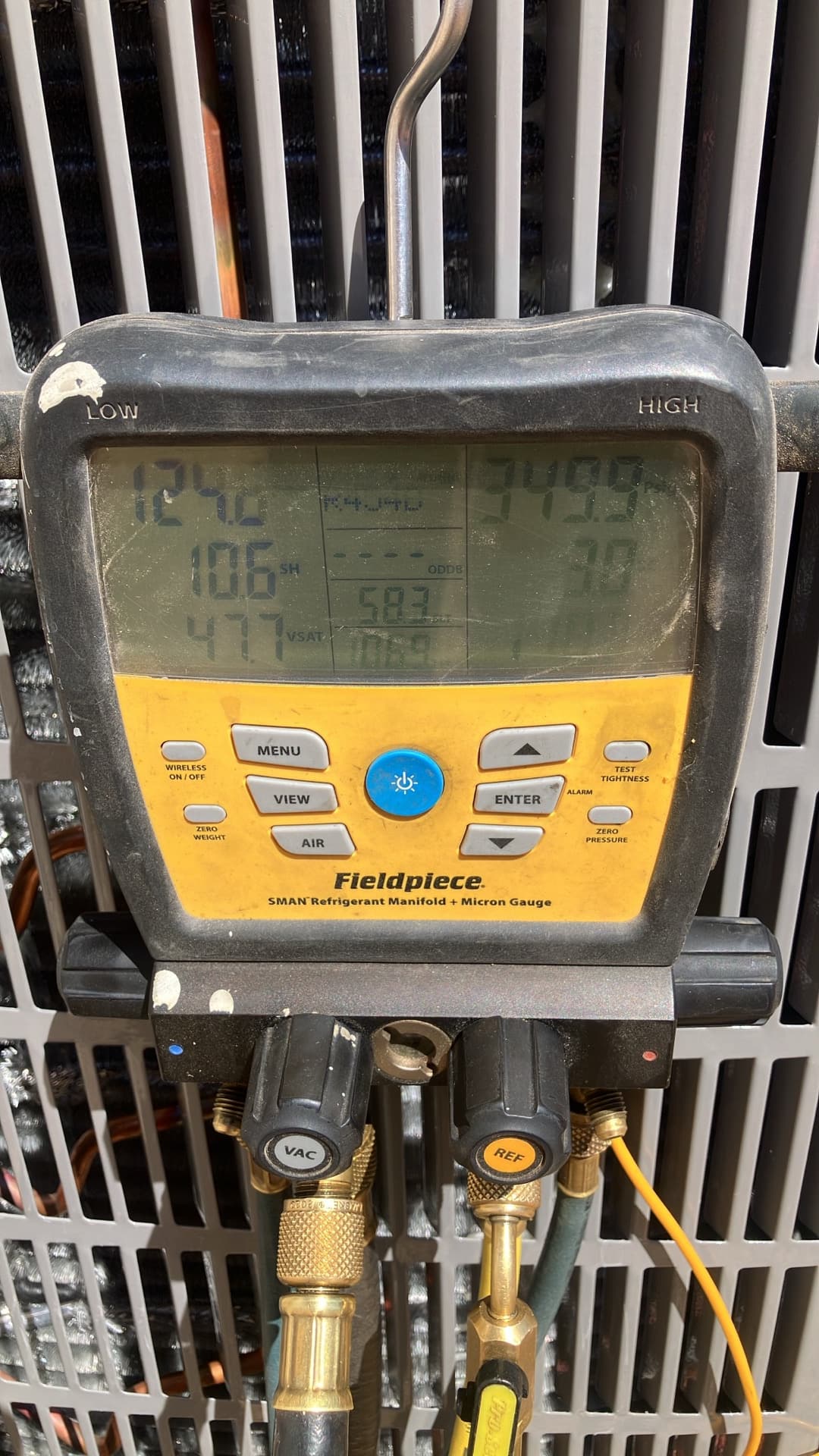 Digital manifold gauge connected to the outdoor unit shows operating pressures with superheat and subcooling during system commissioning.