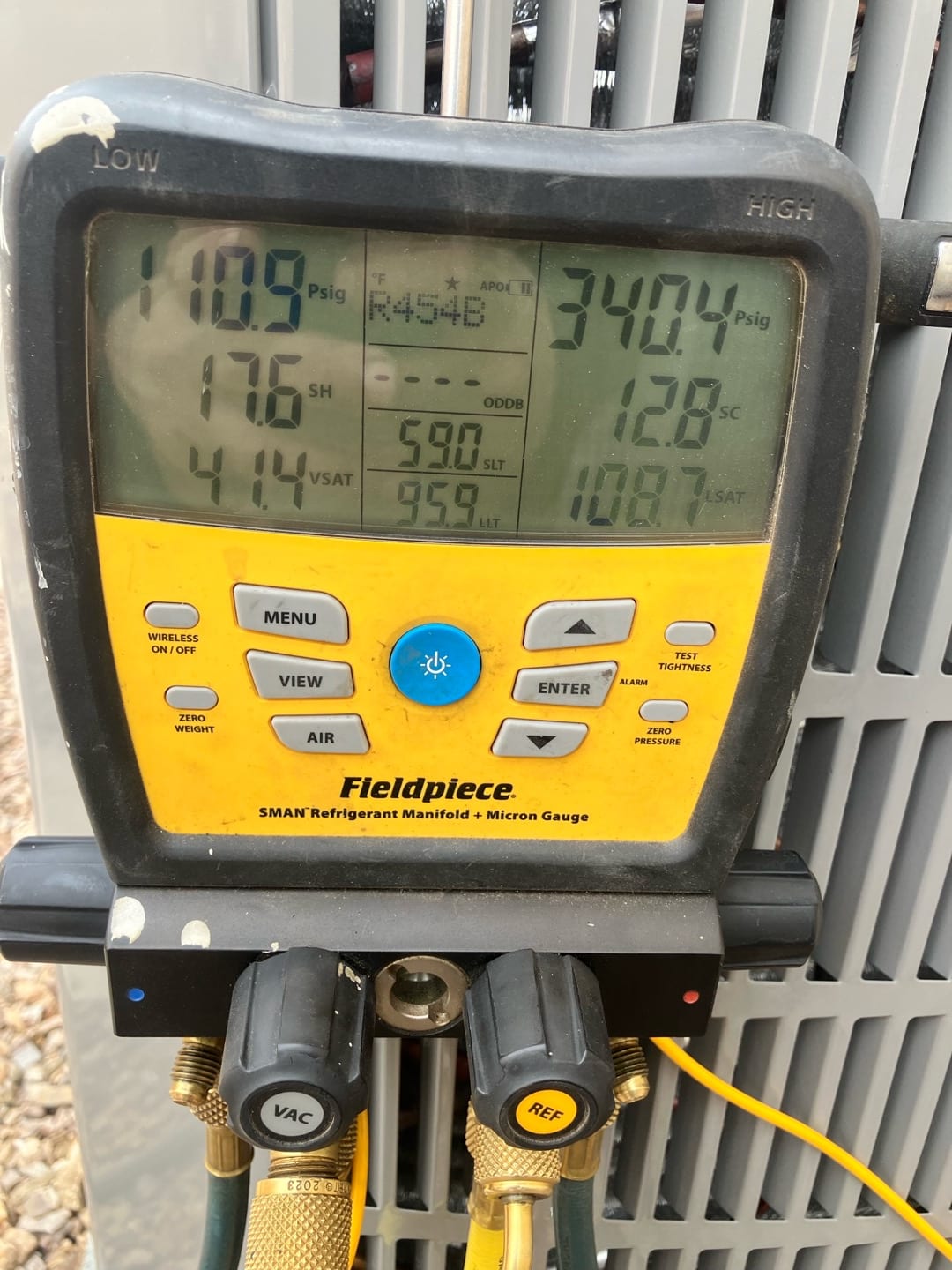 Digital manifold on the outdoor unit shows operating pressures and temperatures during system commissioning with refrigerant connected.