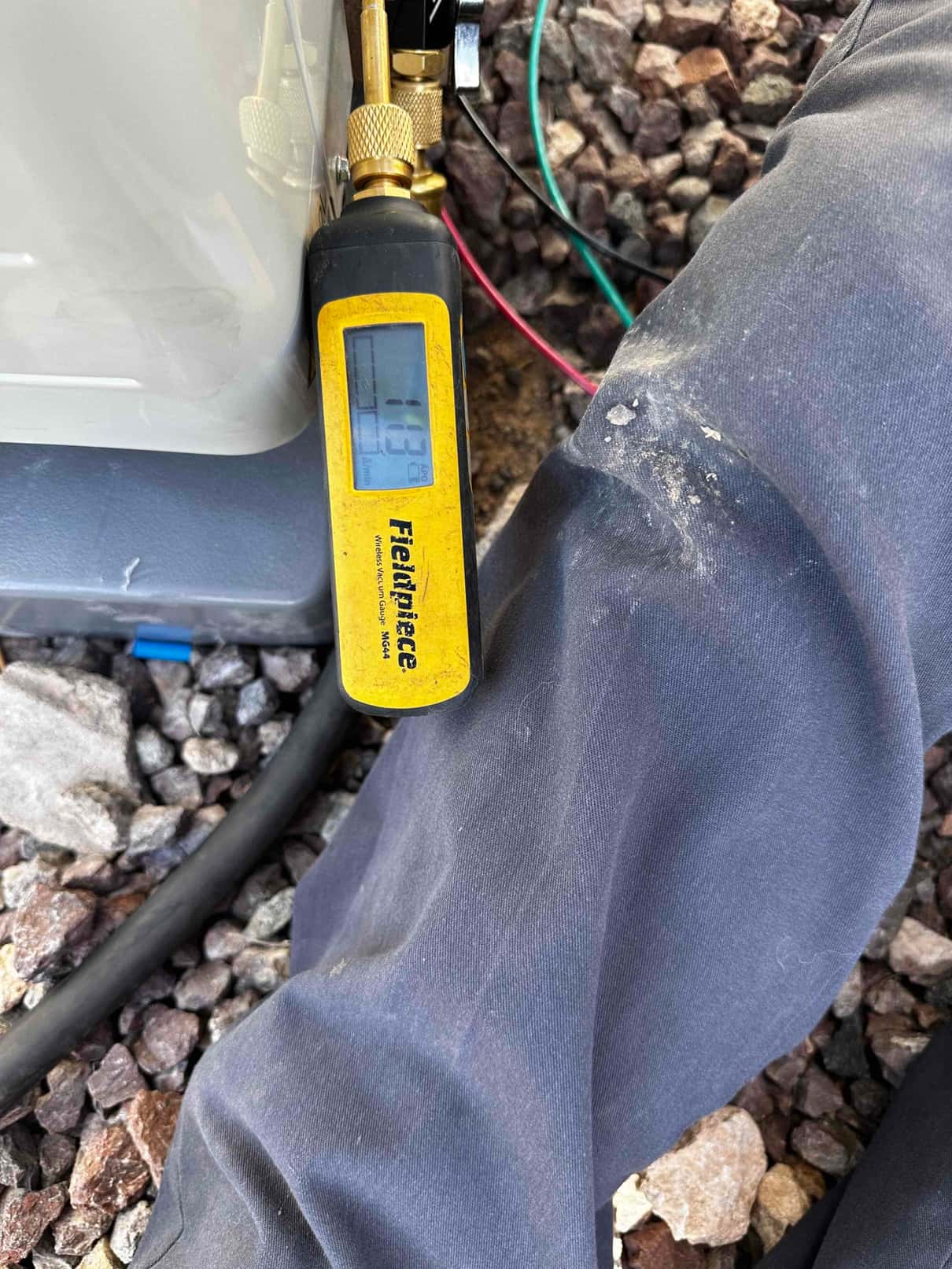 Digital micron gauge connected at the outdoor unit reads 113 microns, confirming a deep vacuum before releasing refrigerant.