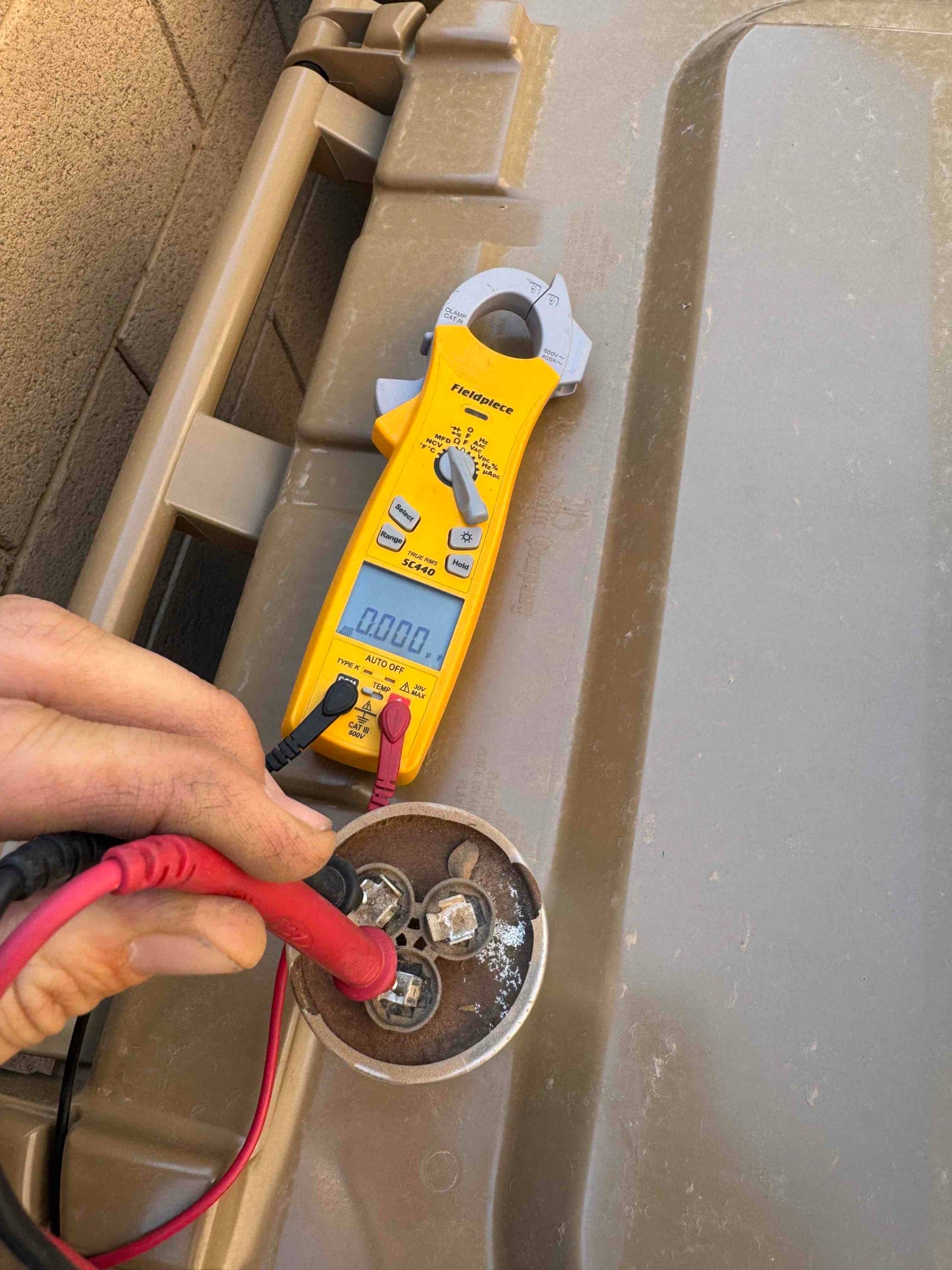 Digital multimeter set to volts shows 0.000 V while test leads contact the capacitor terminals.