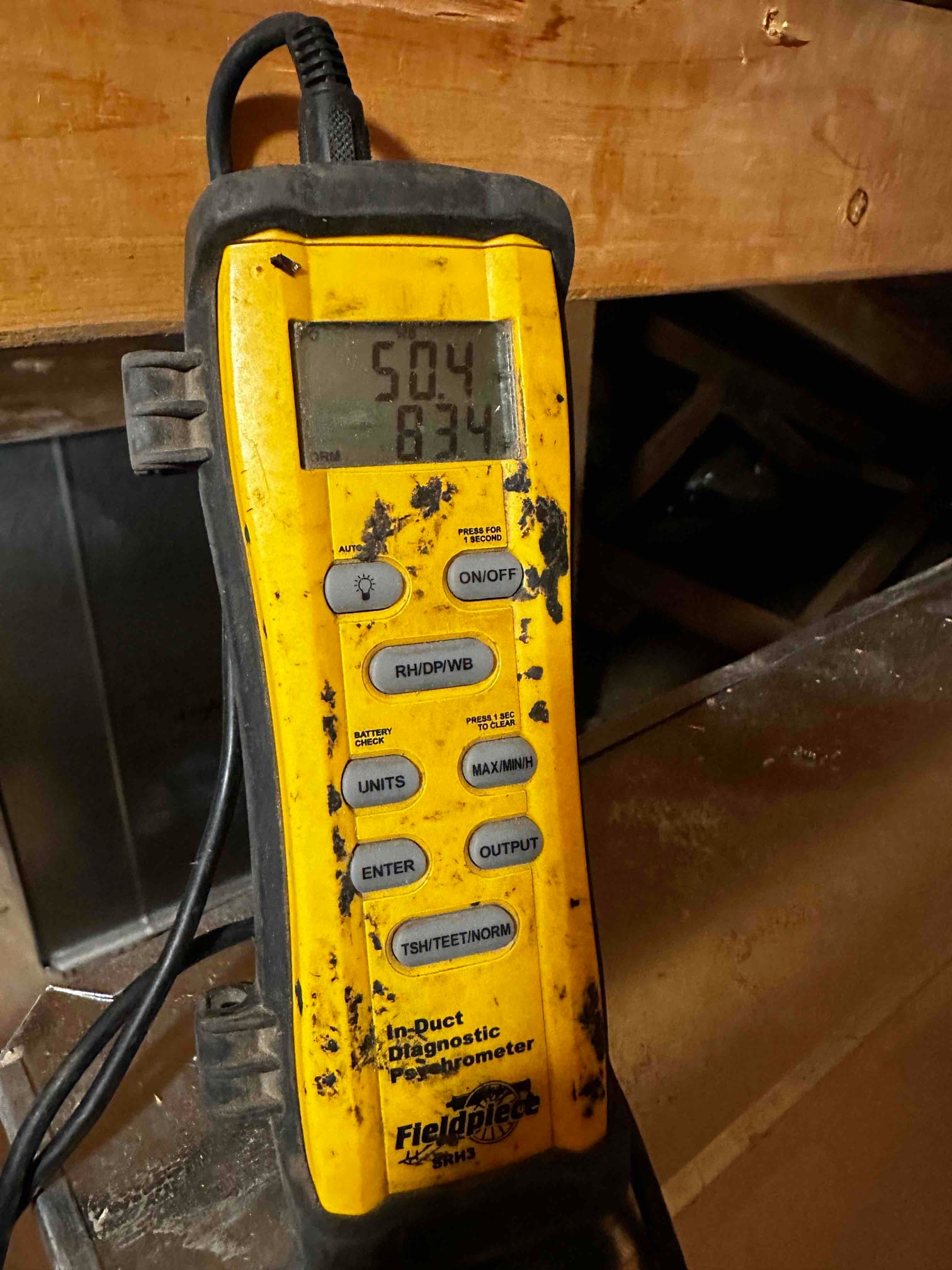 Digital probe thermometer shows 50.4 degrees on the display while measuring air temperature at the duct during commissioning.