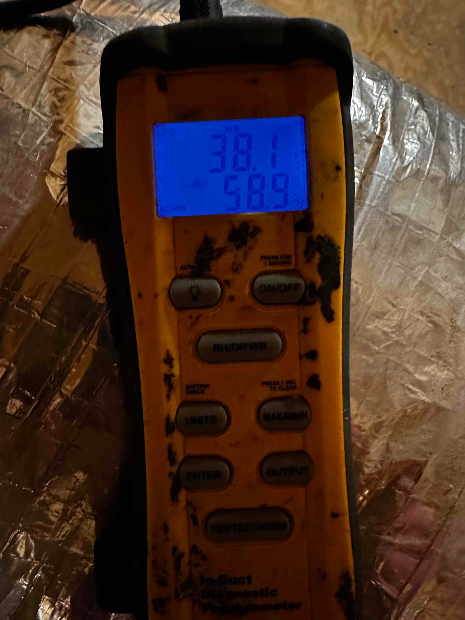Digital thermometer displays 58.9 degrees Fahrenheit while checking air temperature near insulated duct during commissioning.