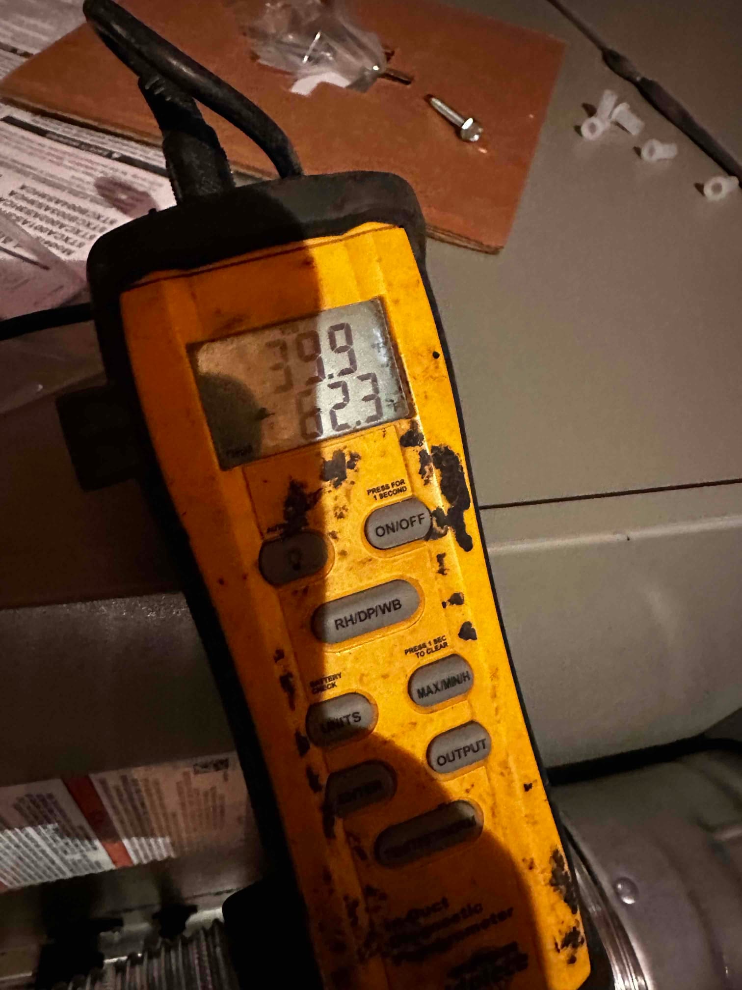 Digital thermometer displays air temperatures during commissioning inside the air handler area to document supply and return conditions.
