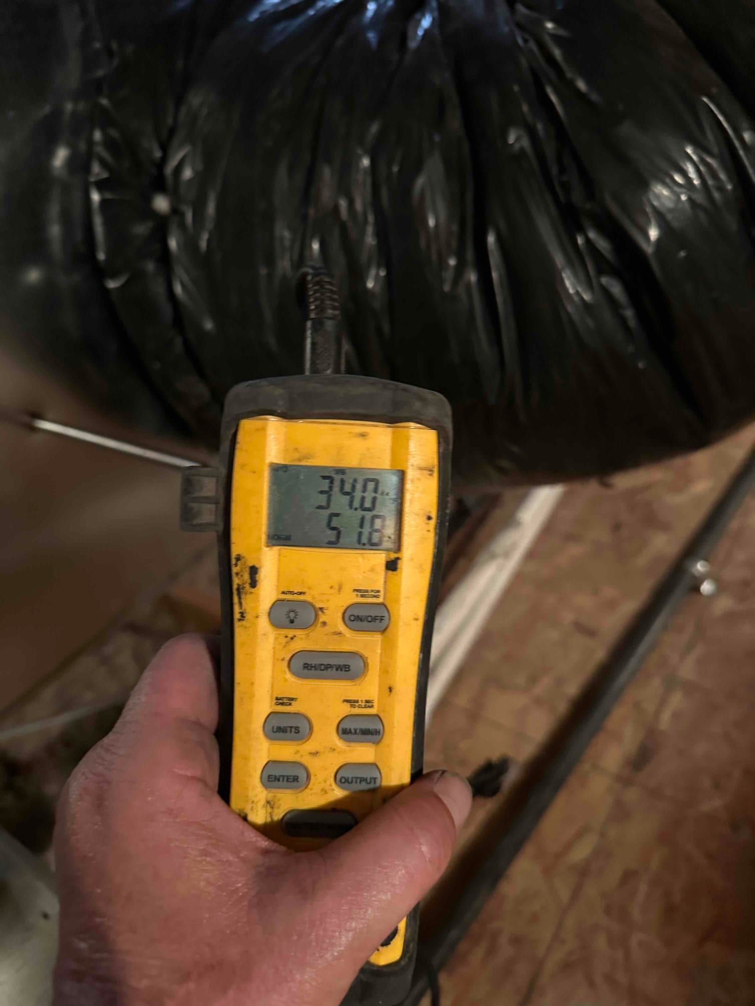 Digital thermometer probe inserted into flexible duct shows 51.8 degrees Fahrenheit, documenting cooled supply air during commissioning.