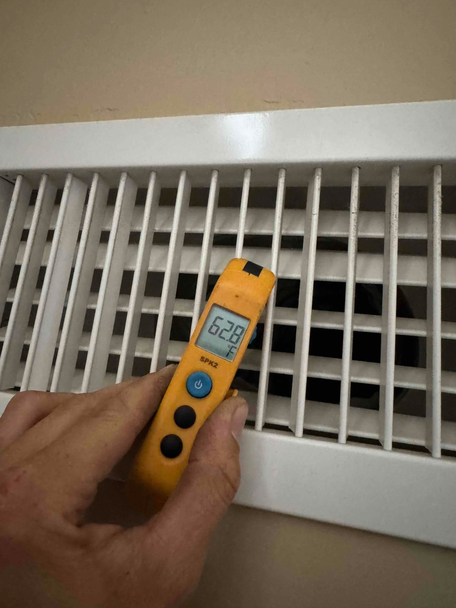 Digital thermometer shows 62.8 °F at the supply air register, with the probe inserted through the grille.