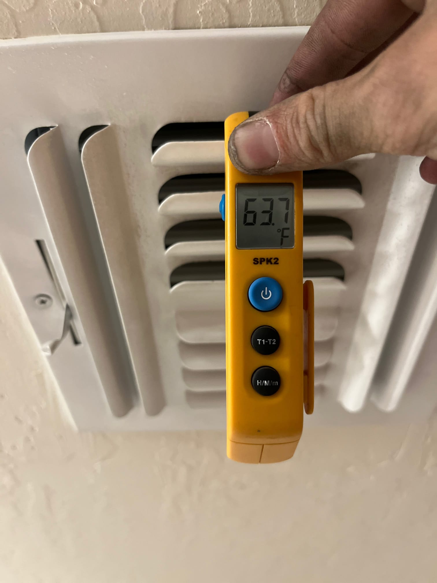 Digital thermometer shows 63.7 °F at a supply air register during air conditioning operation.