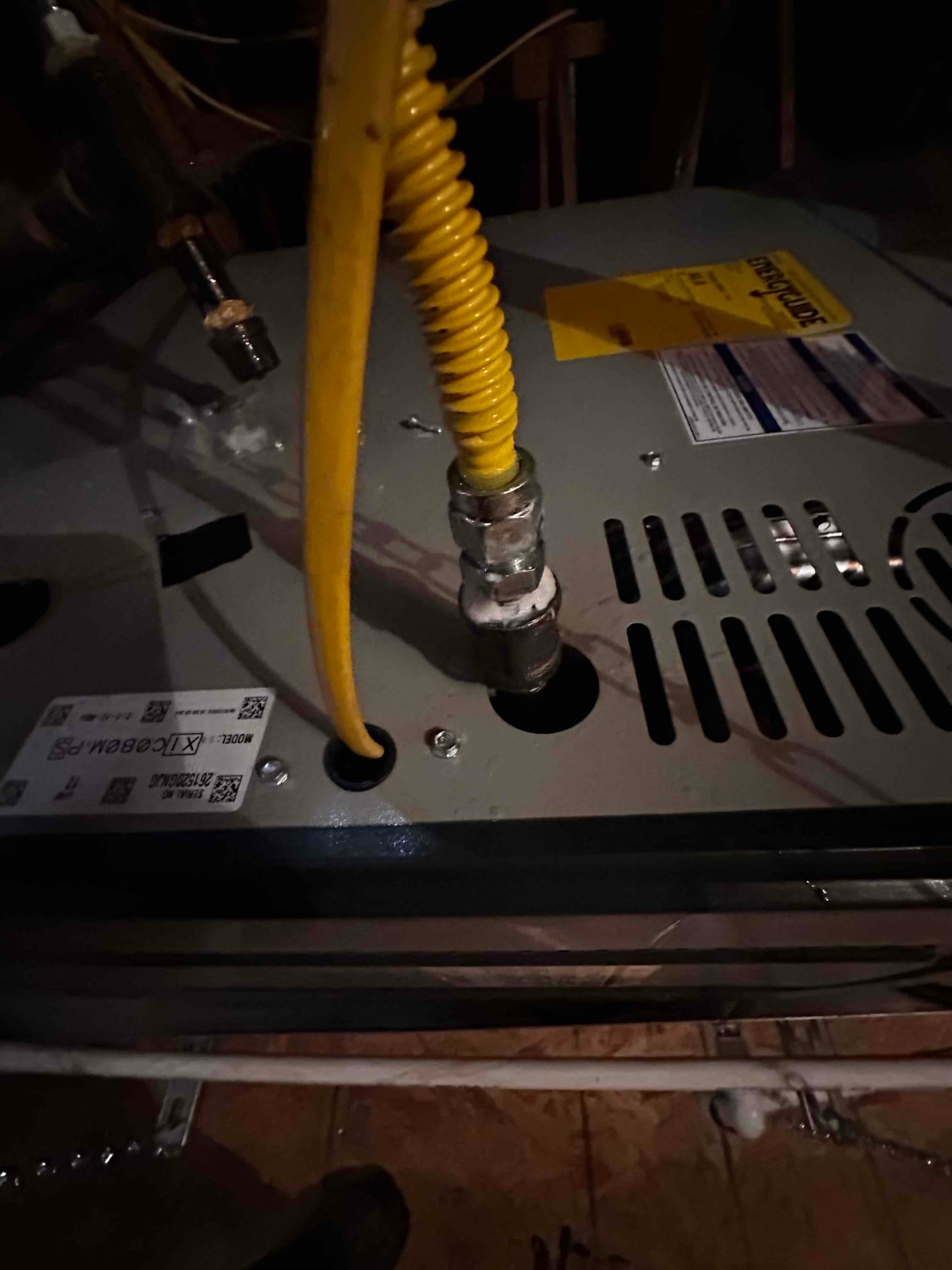 Flexible gas connector routed into the furnace cabinet with secured fittings and knockout grommet visible during installation.